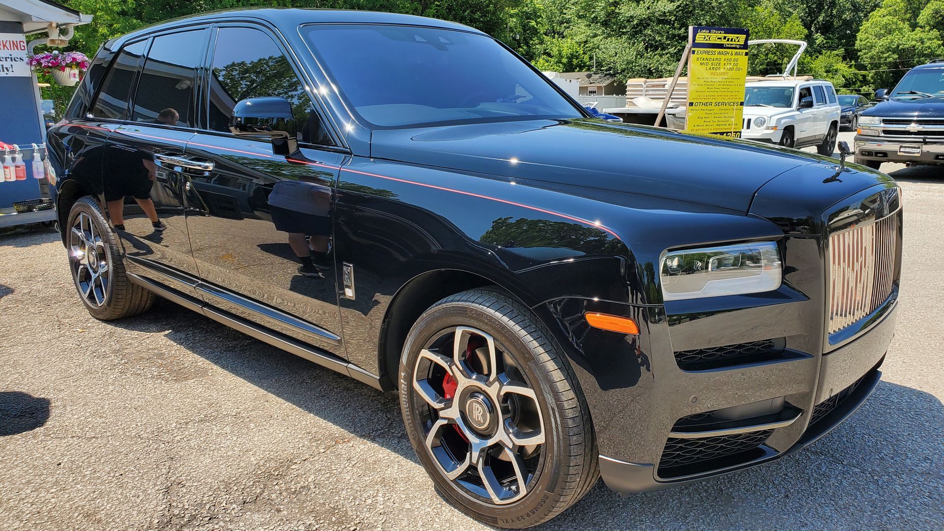 A black rolls royce cullinan is parked in a gravel lot.