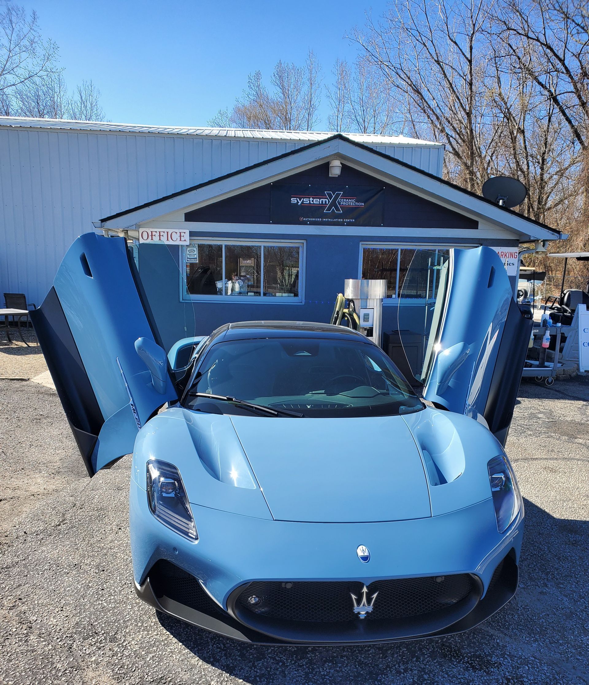 A blue maserati with its doors open is parked in front of a building.
