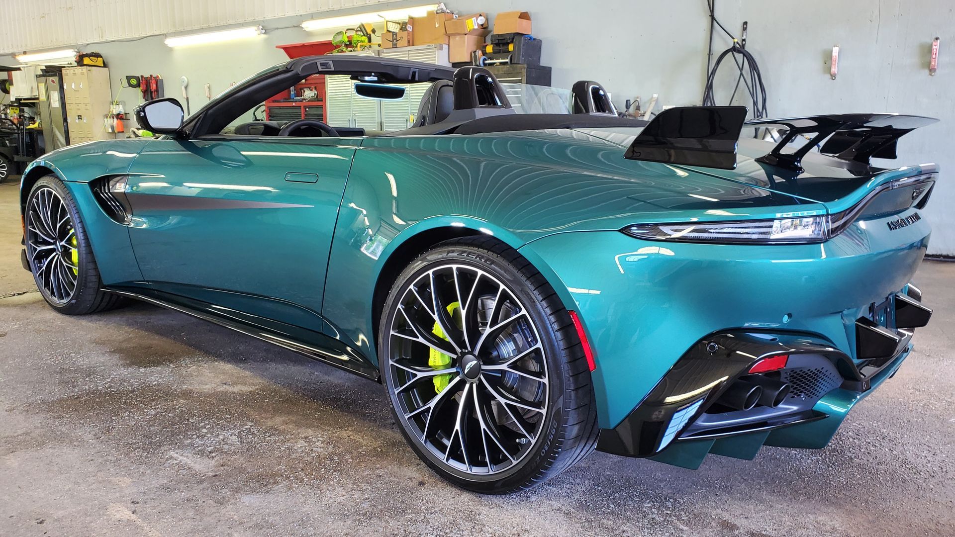A green sports car with a convertible top is parked in a garage.