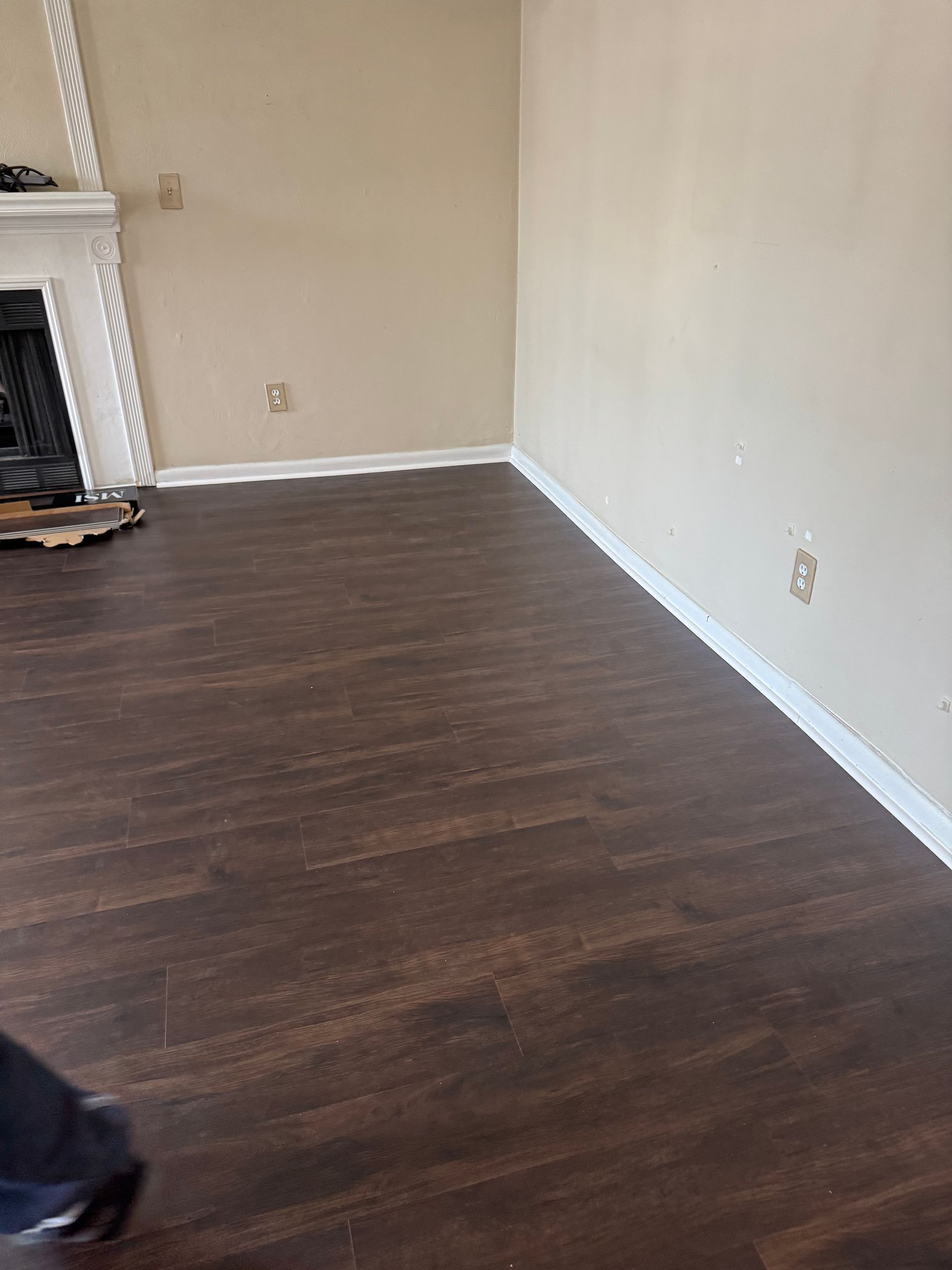 Empty living room with dark wood flooring, white walls, and a fireplace on the left.