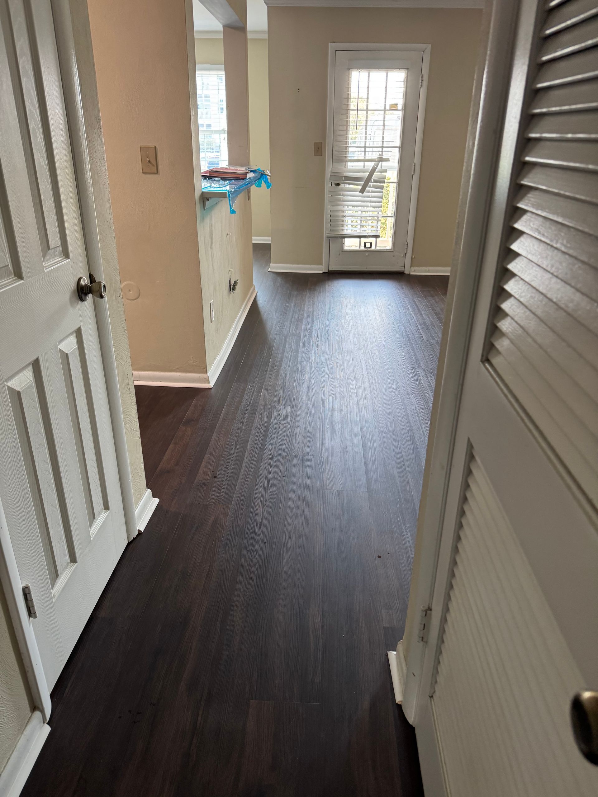 Narrow hallway with dark wood floor, beige walls, and a glass door at the end.