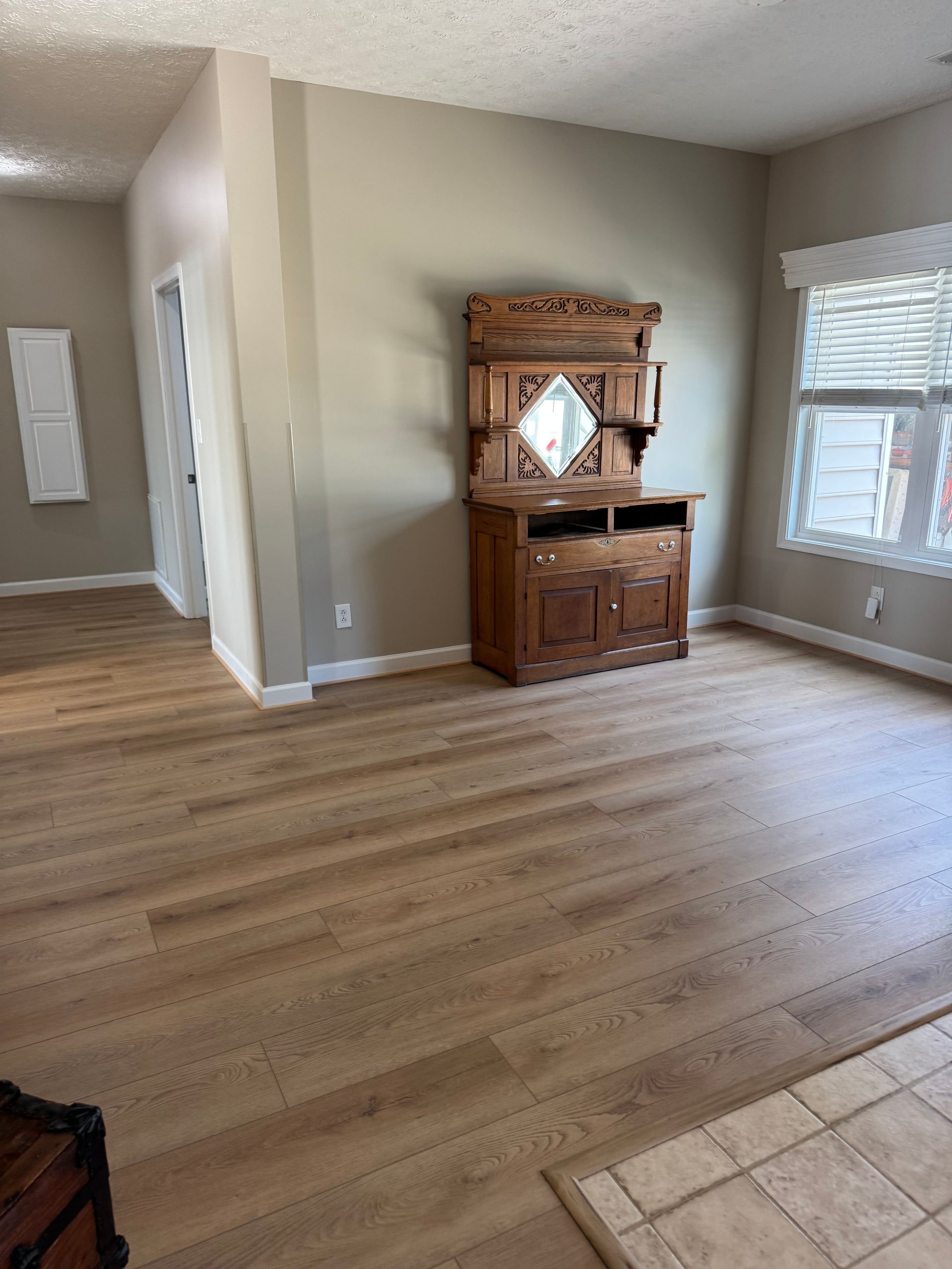 Empty living room with wood floors, beige walls, and a wooden cabinet against the far wall.