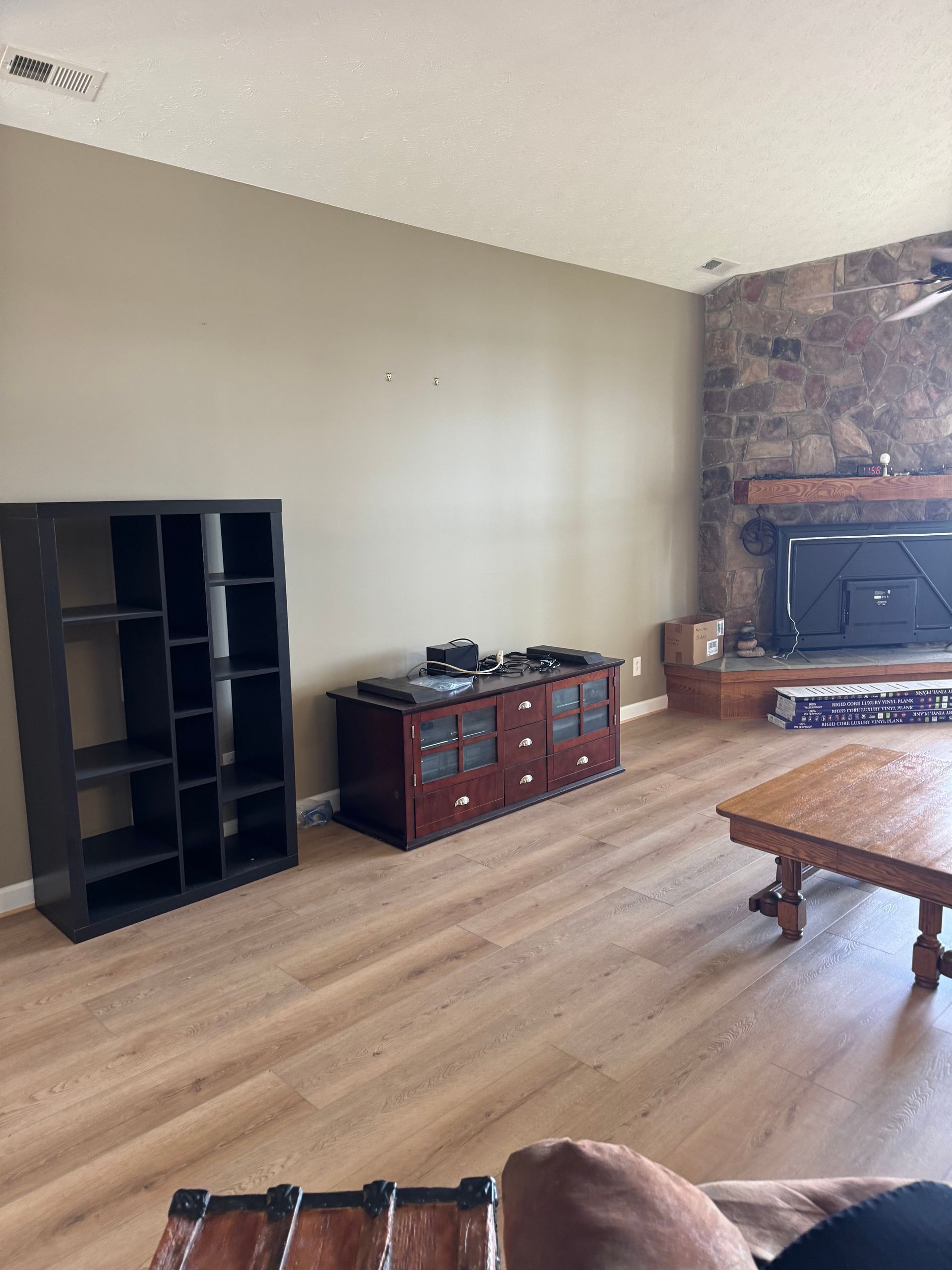 Spacious living room with wood floors, beige walls, black shelf, red cabinet, stone fireplace, and coffee table.