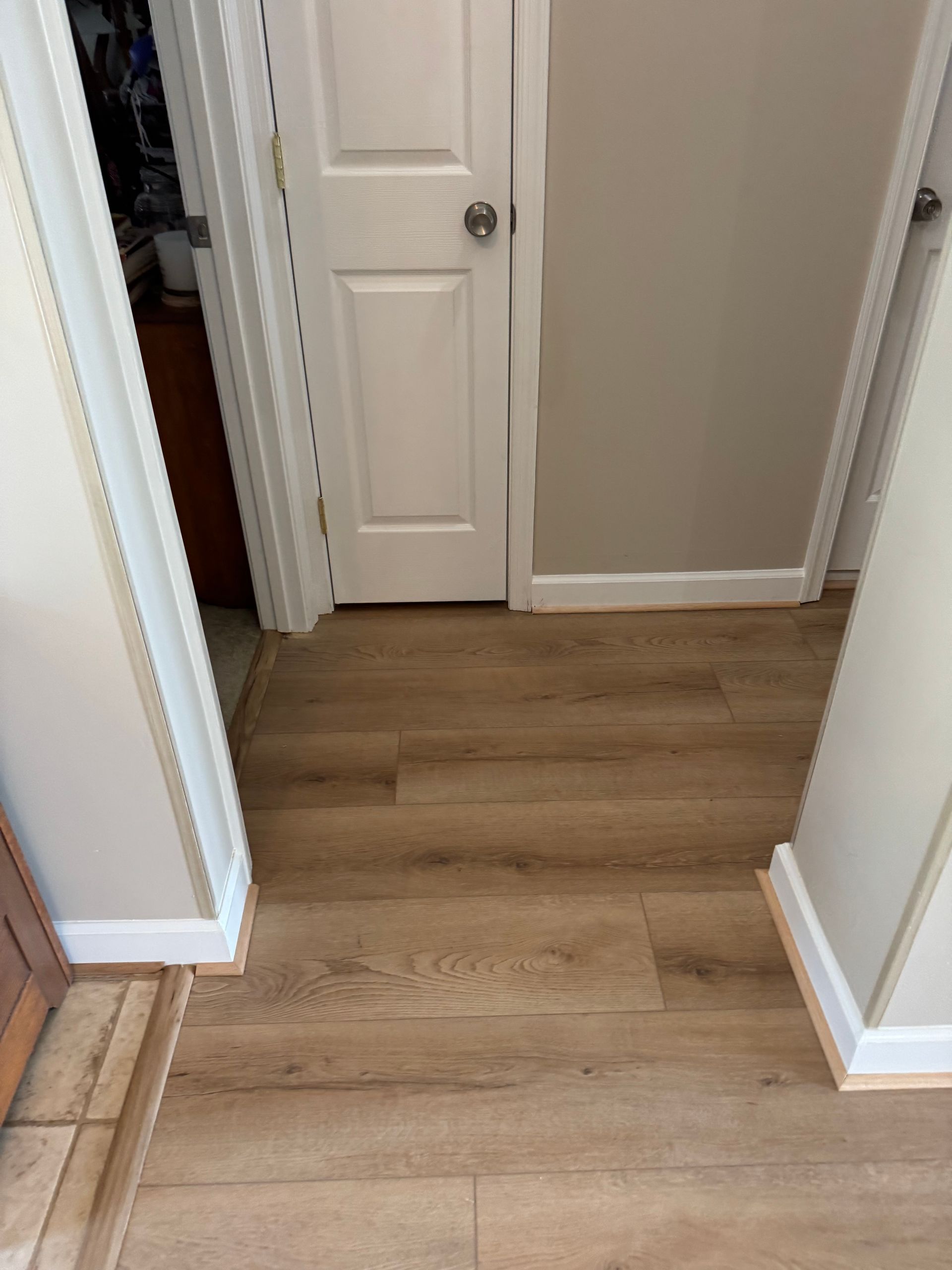 Hallway with light wood flooring and white doors leading to a beige room.