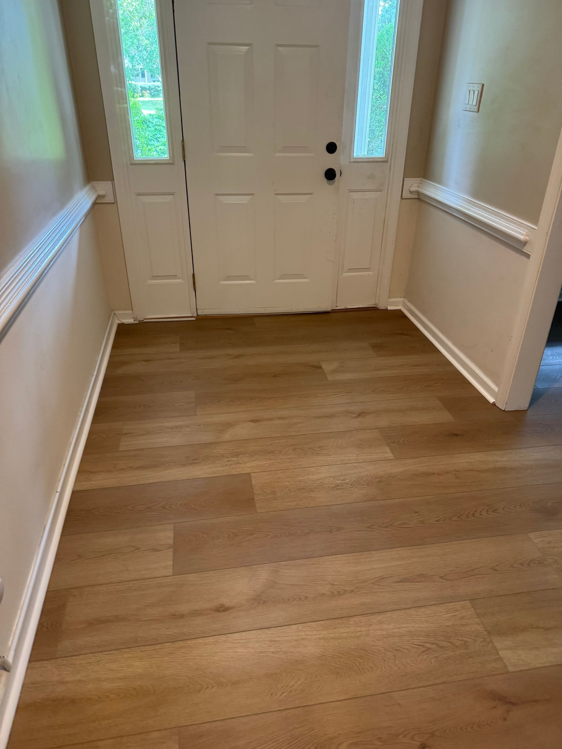 Front entry hall with hardwood floor and white double doors with glass sidelights.