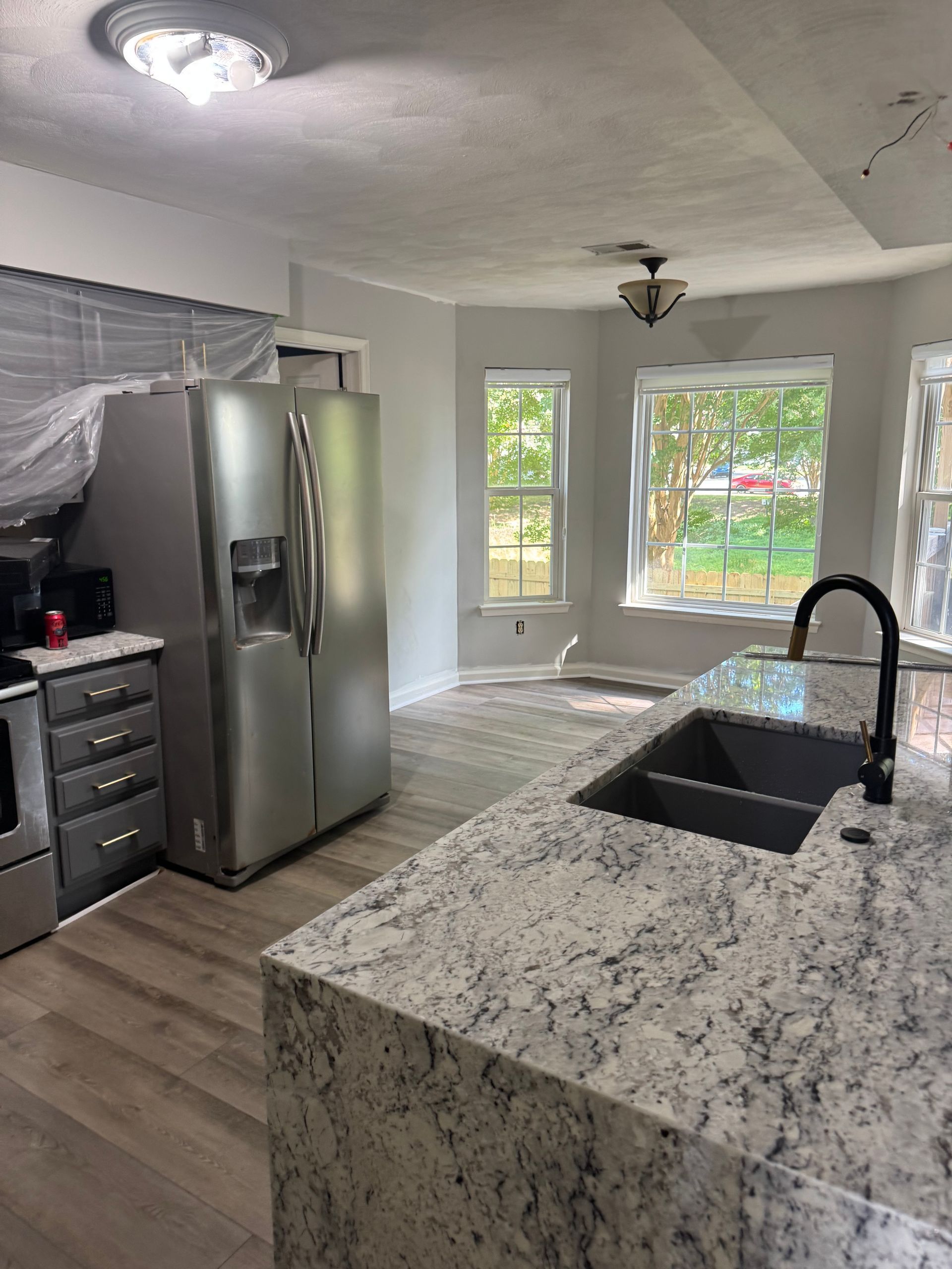 Modern kitchen with stainless steel appliances, granite island, black sink, and bright windows.