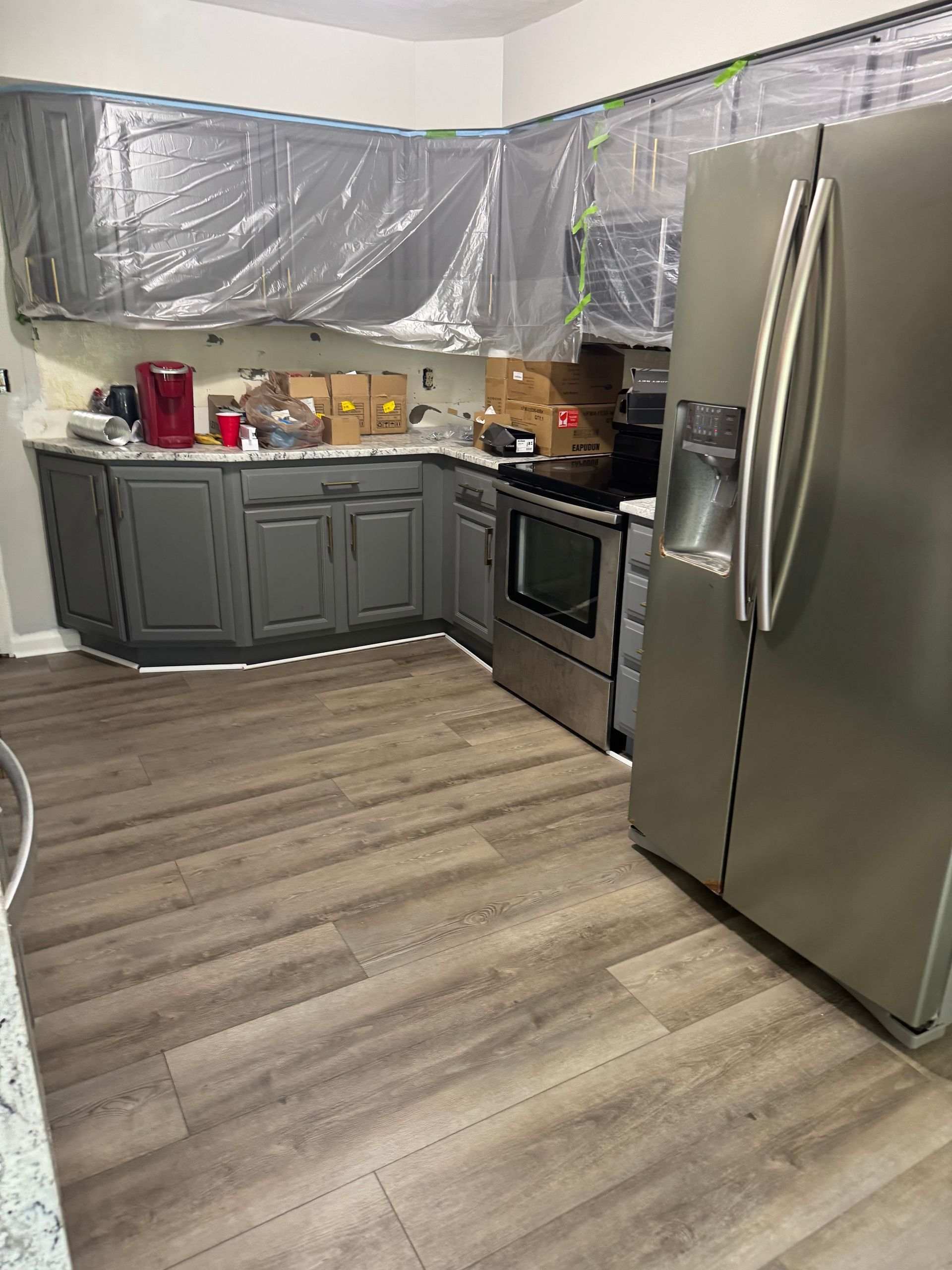 Modern kitchen with gray cabinets, stainless steel fridge and oven, and plastic-covered countertops under renovation