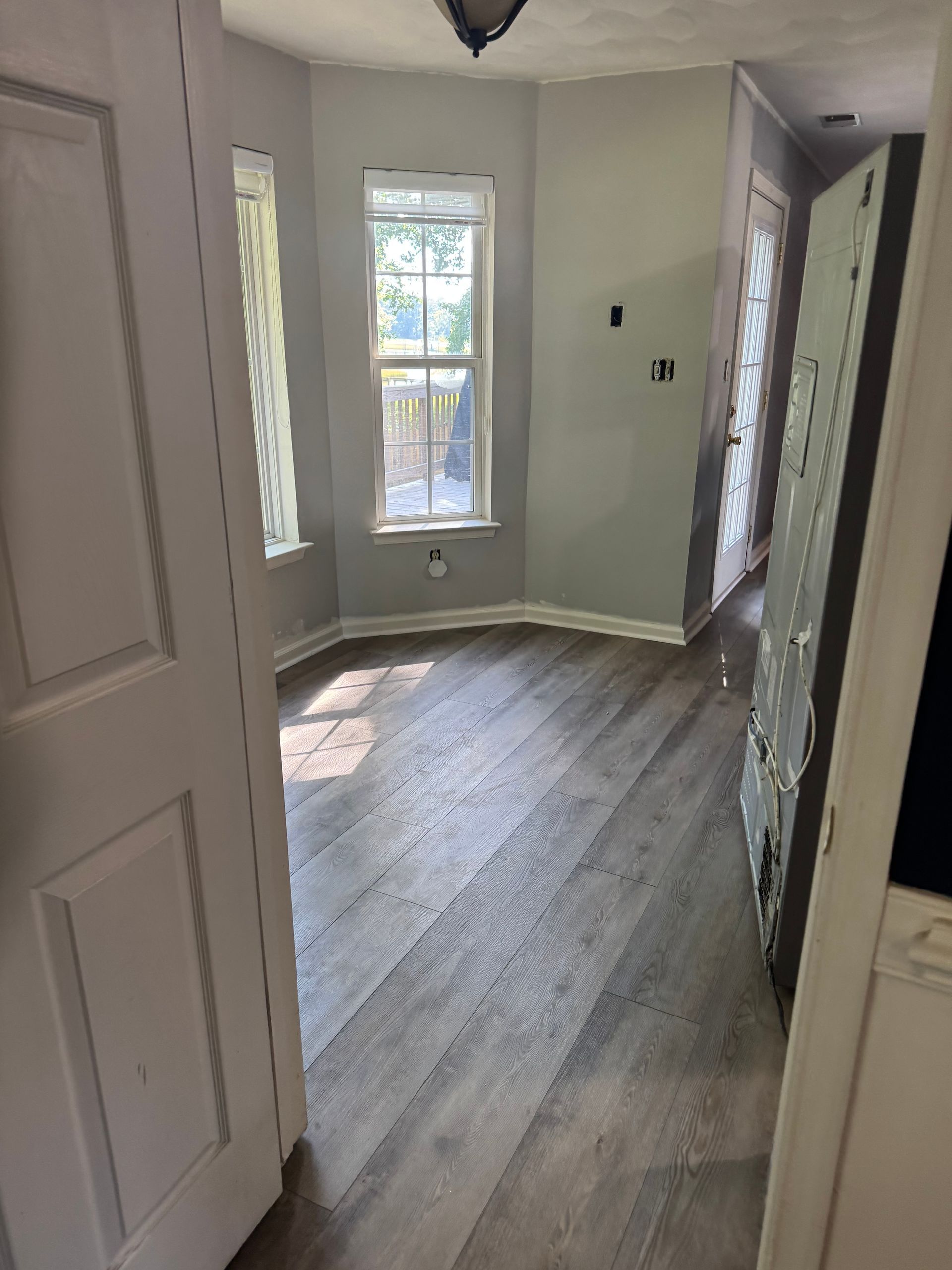 Empty hallway with new wood floors, white walls, and two windows letting in daylight.