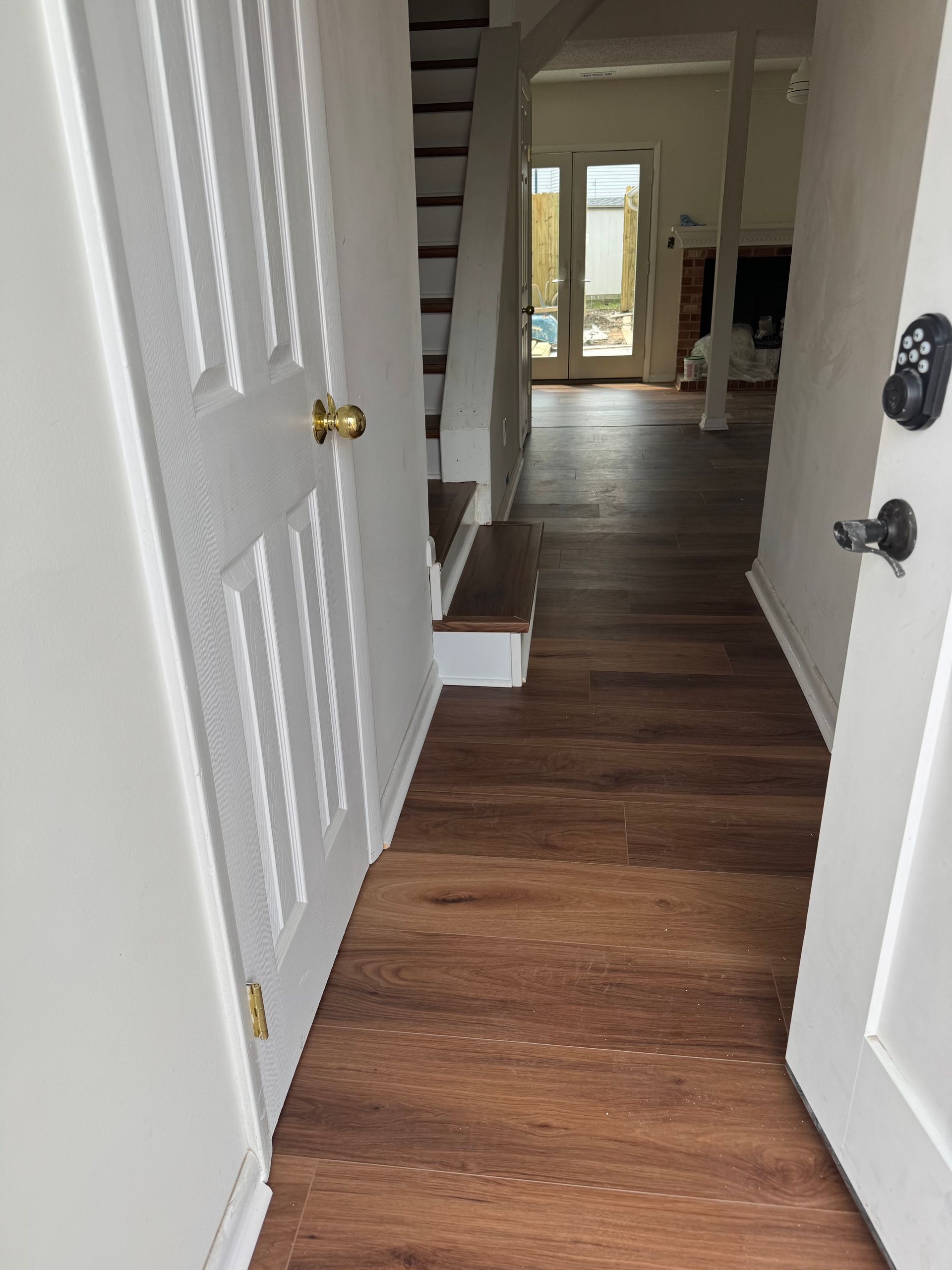 Hallway with wood floors, white walls, open doors, and stairs leading to a bright room in the distance