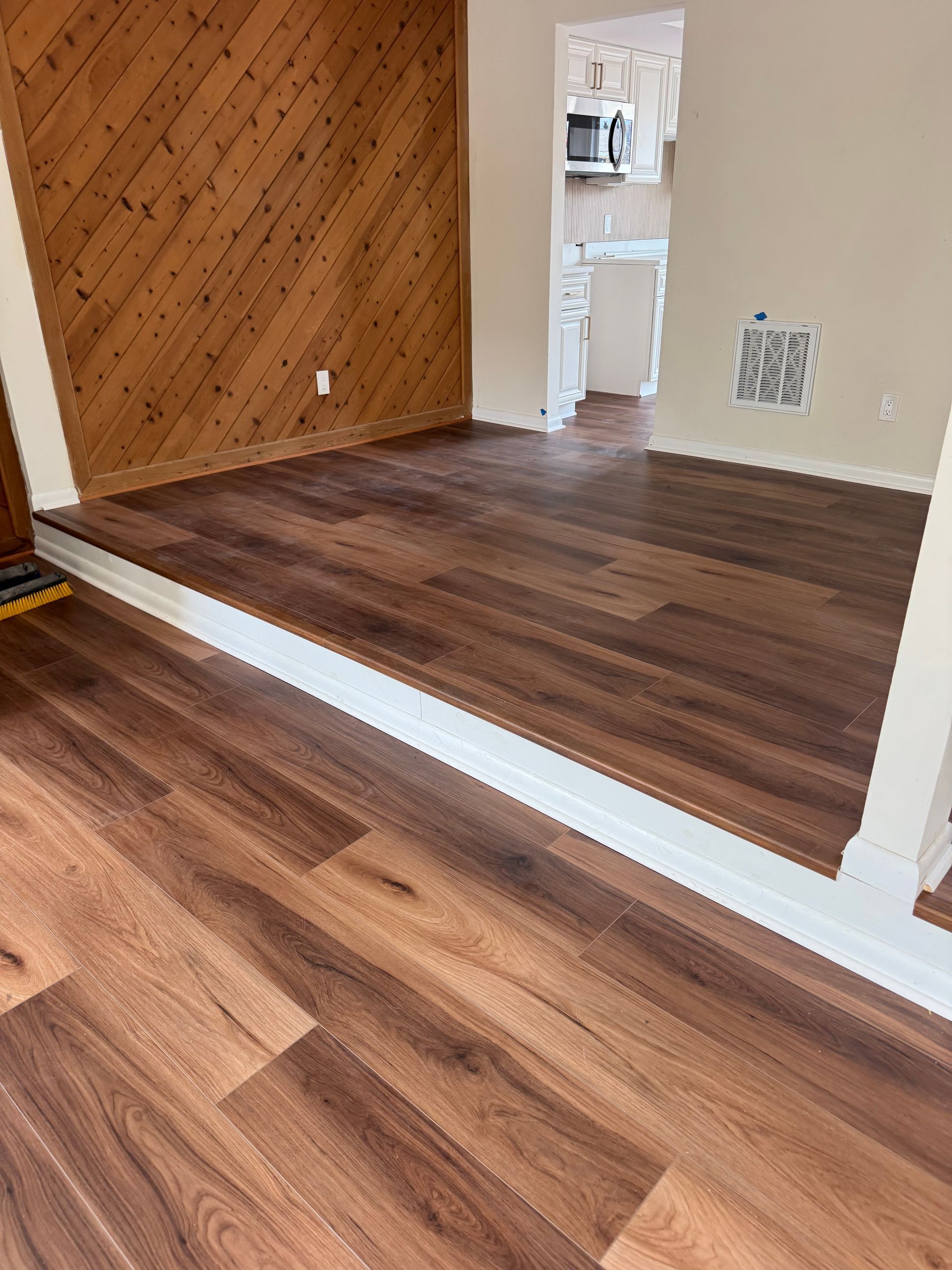 Empty room with wood floors, white trim, and a small open doorway to a sink area.