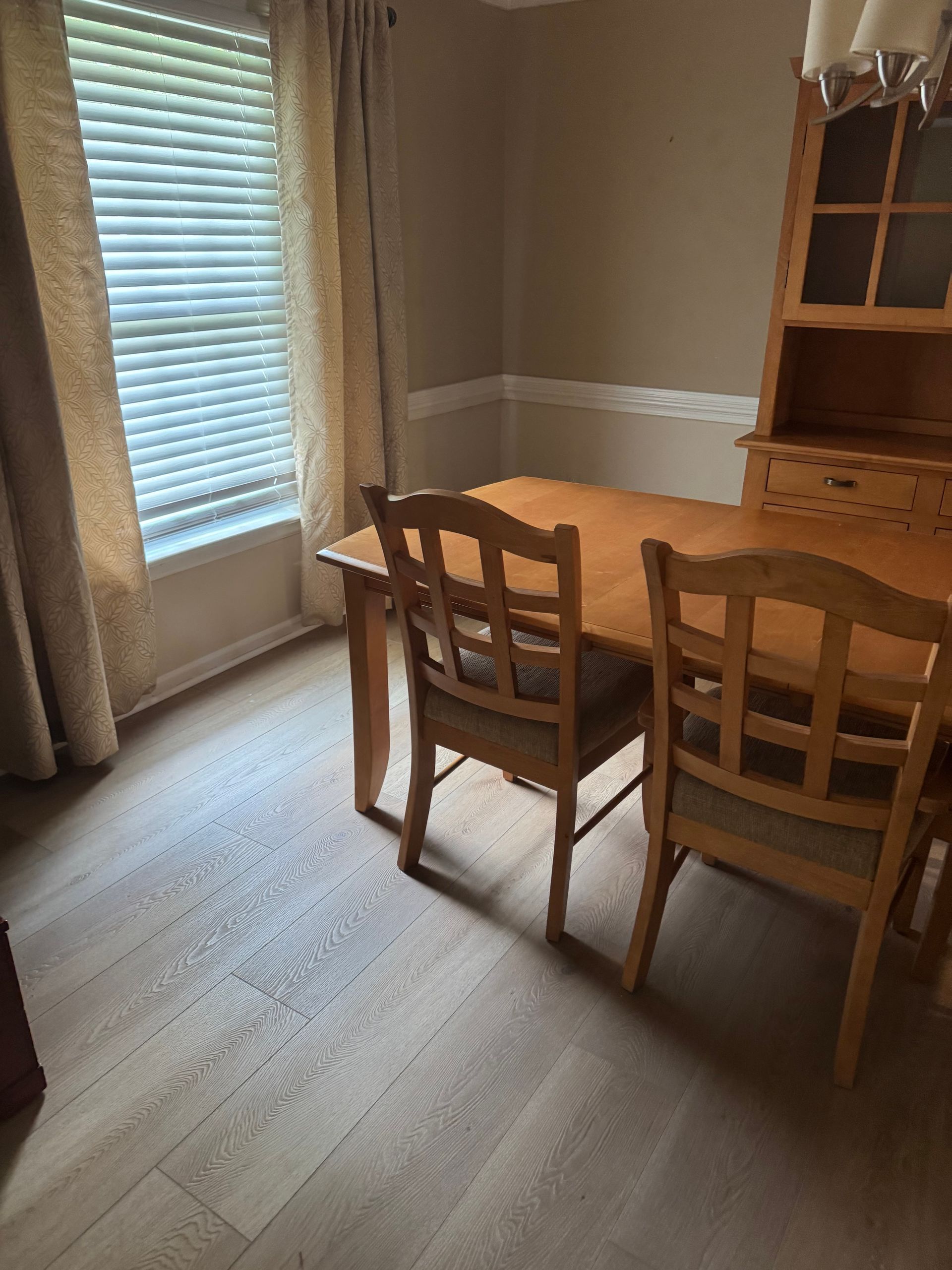 Small dining room with wooden table and chairs beside a window with blinds and curtains.