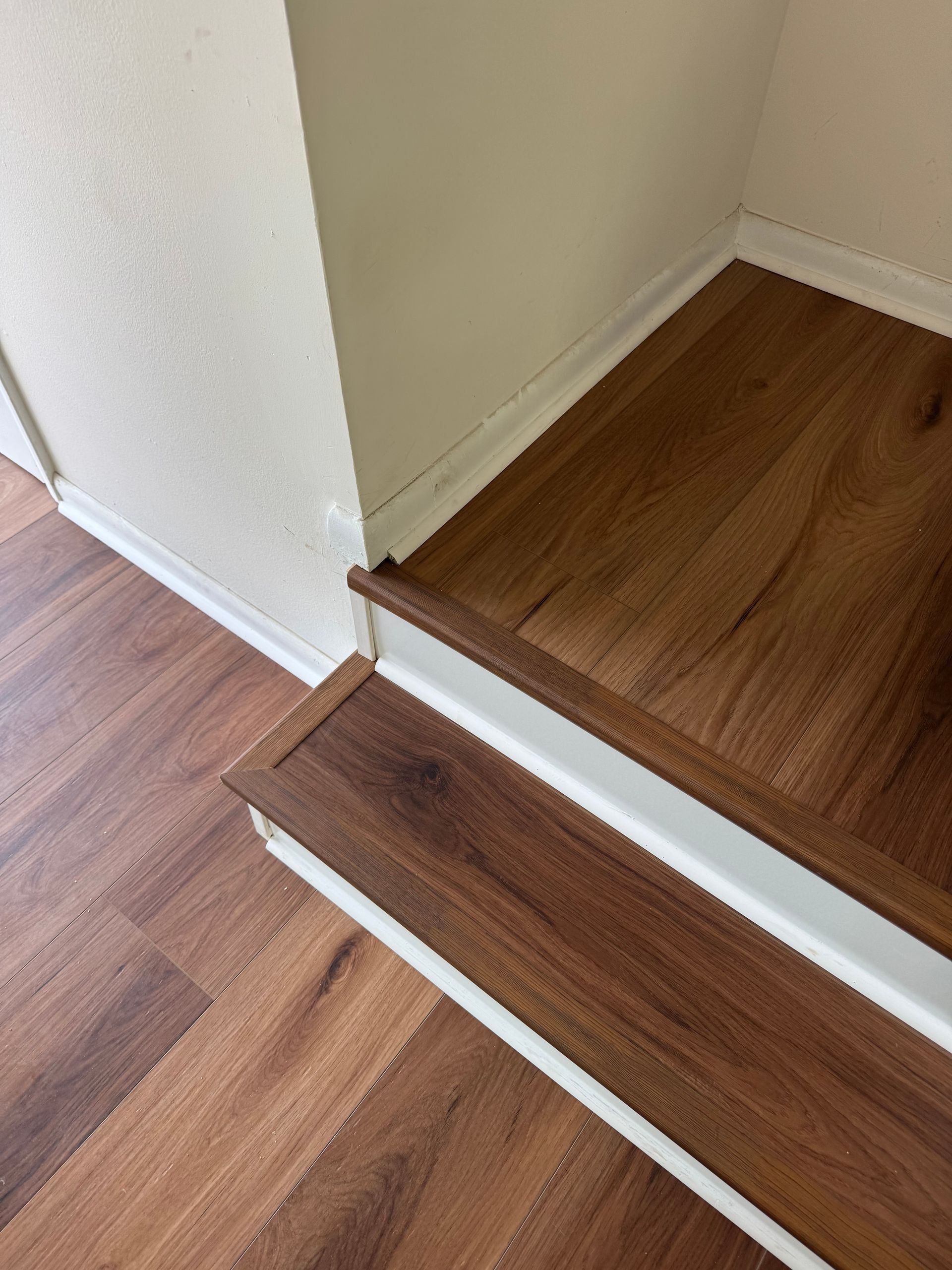 Wooden staircase steps beside a hardwood floor and white wall corner