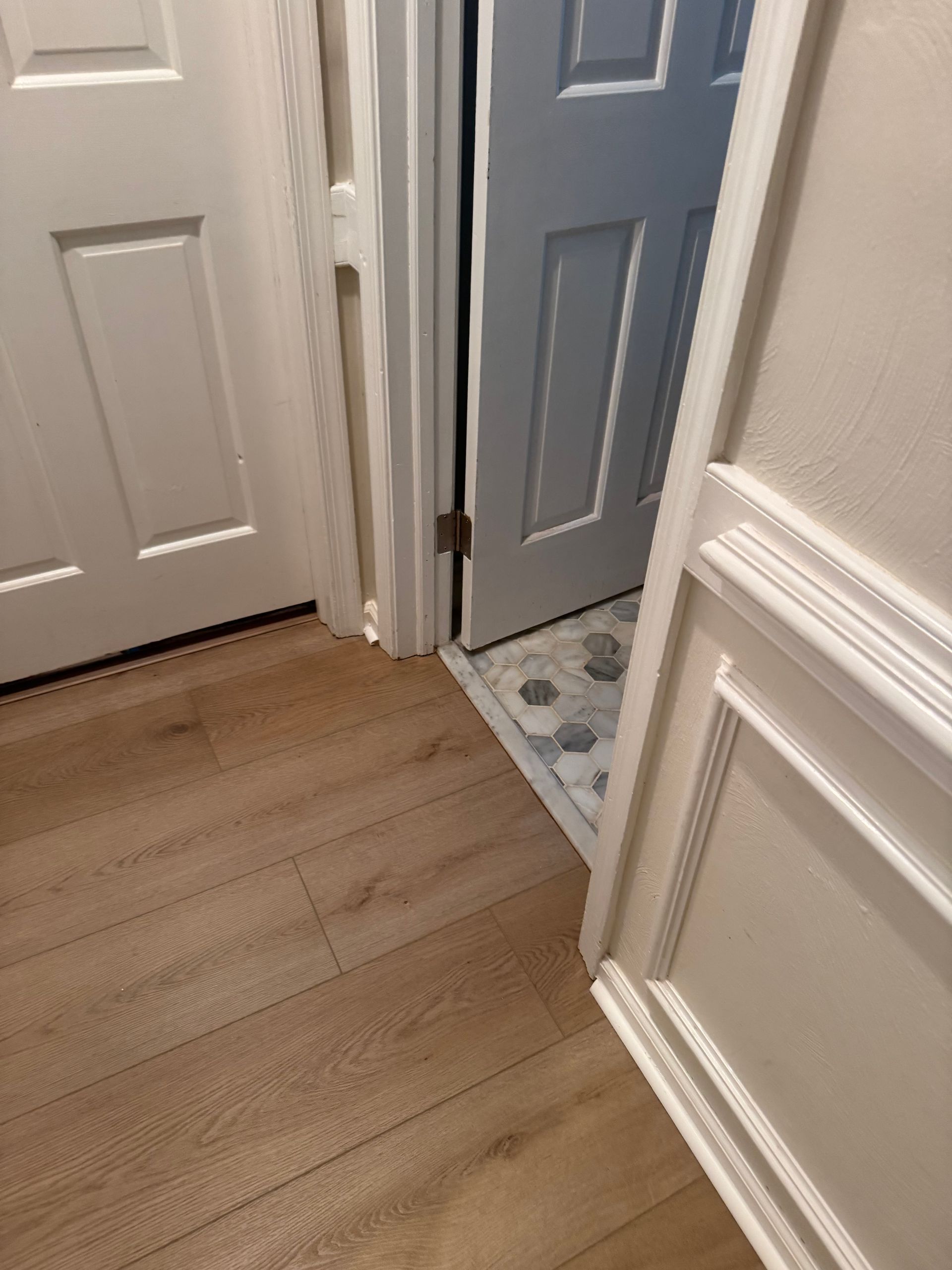 Hallway with hardwood floor, open white and blue doors, and a small tiled bathroom area.
