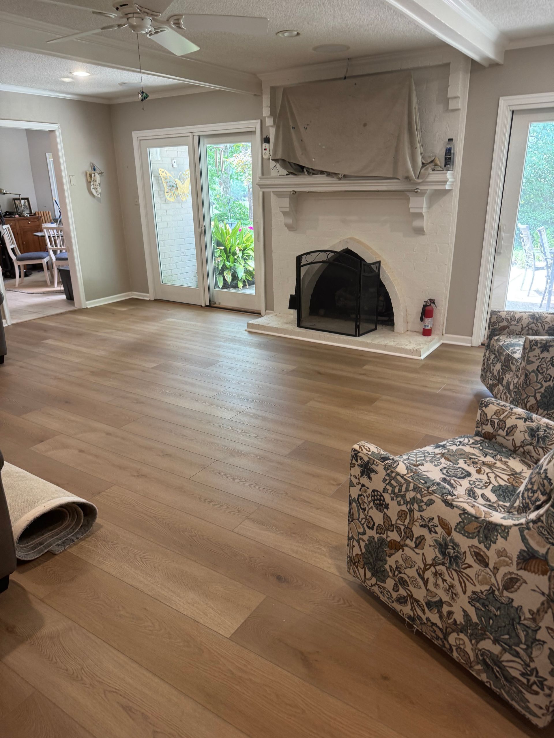 Empty living room with hardwood floors, white fireplace, French doors, and floral armchair