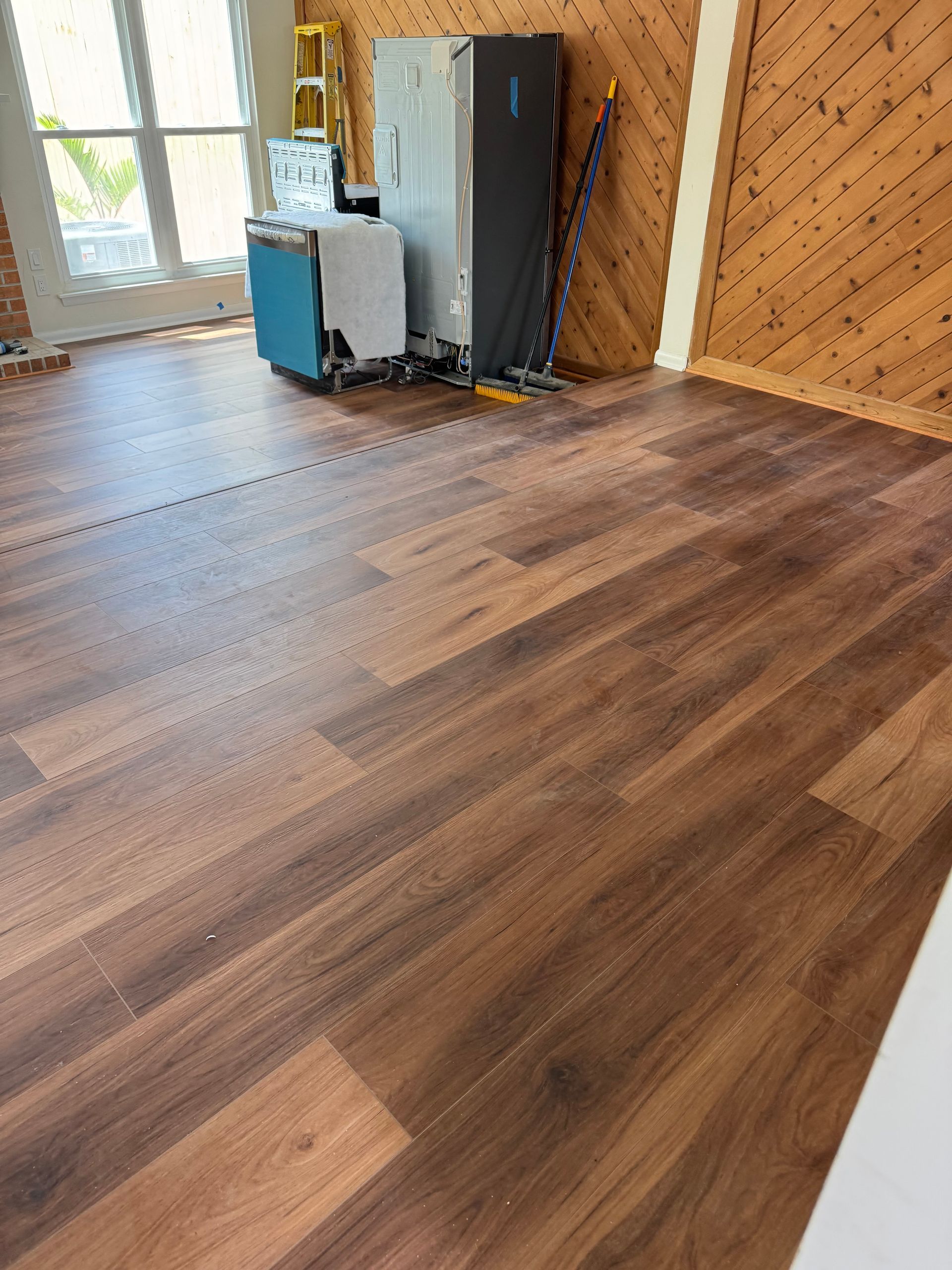 Empty room with wood-look flooring, a window, and a gray cabinet against unfinished wood walls.