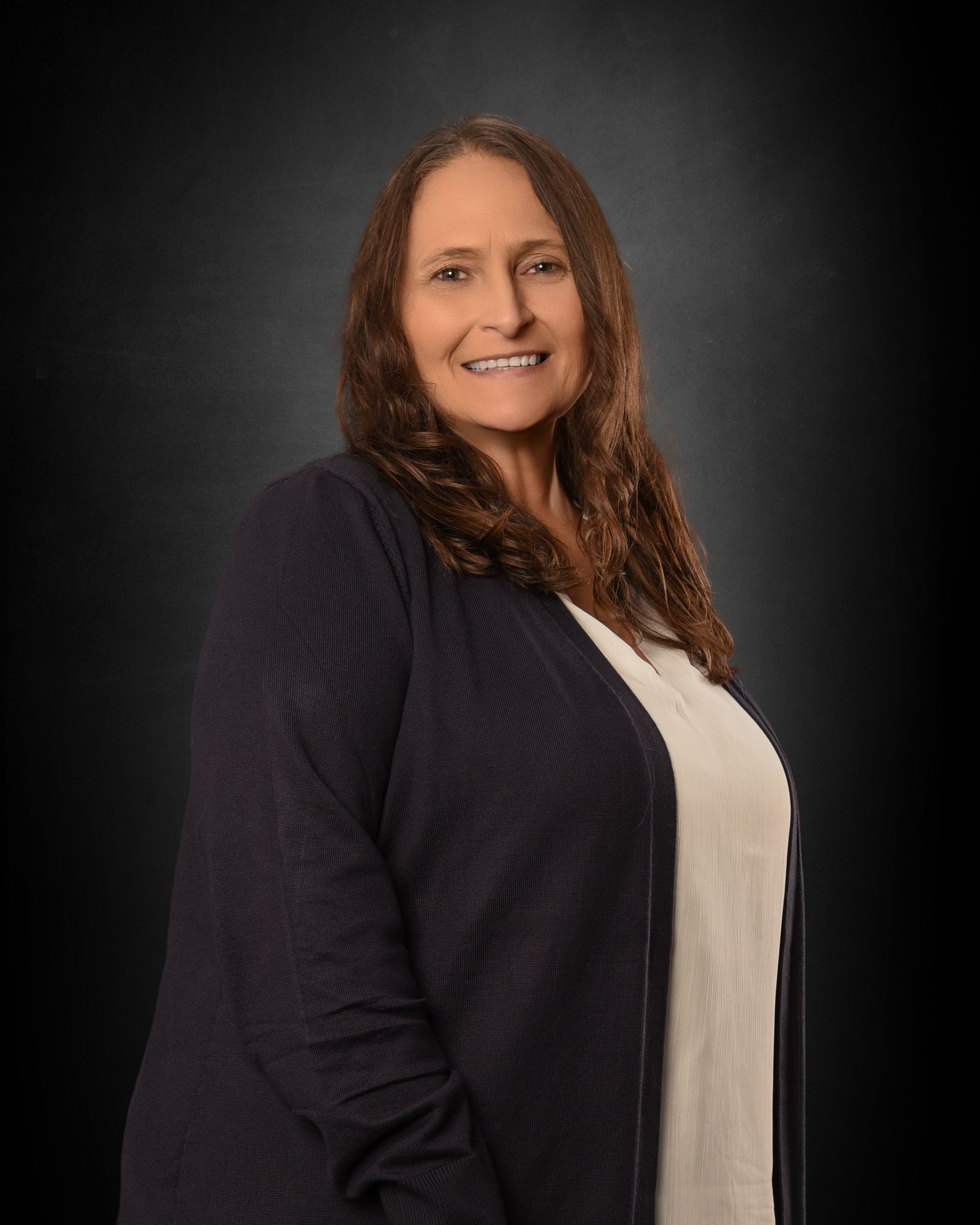 Smiling person in a dark cardigan and white top against a black background