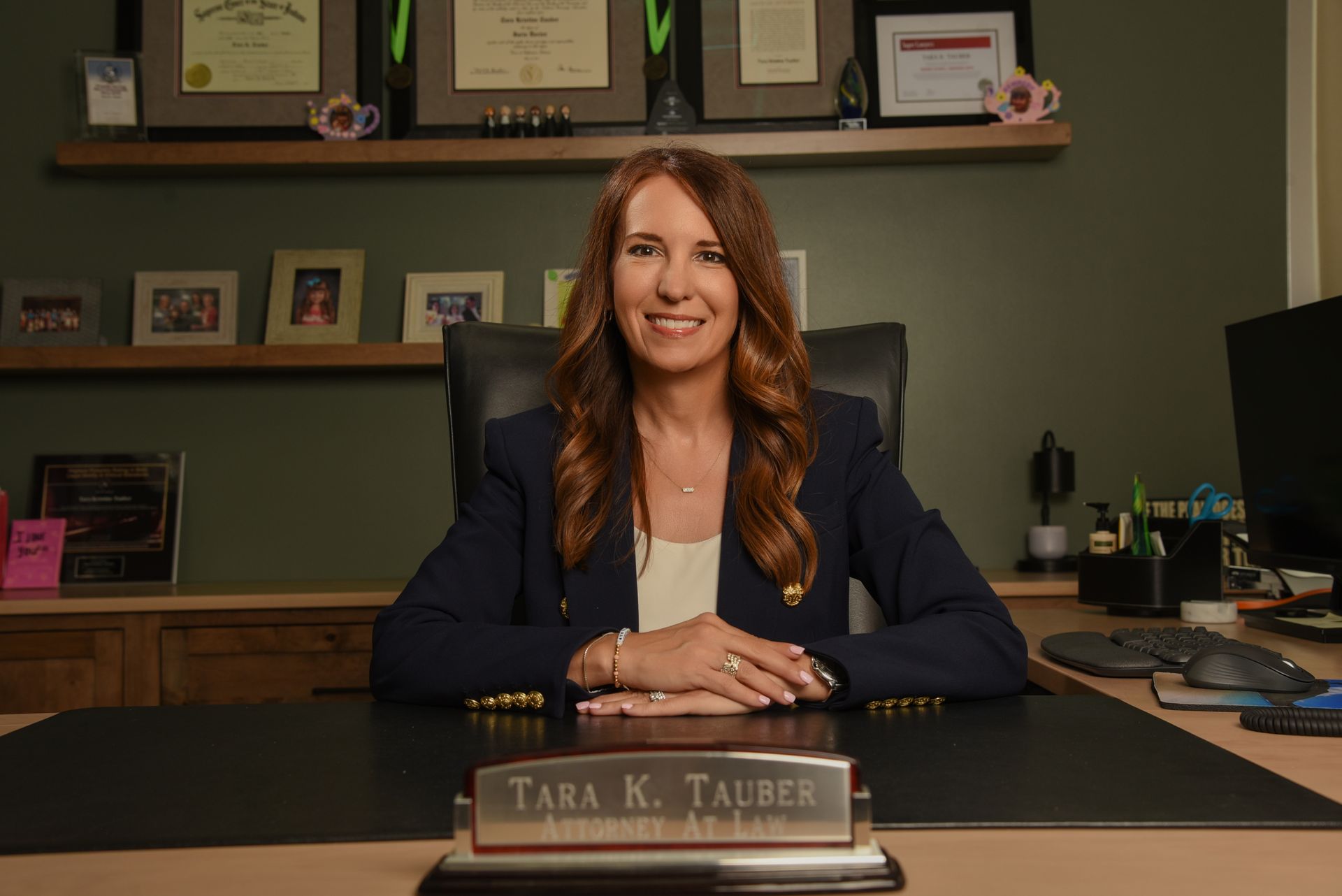 Smiling woman seated at a desk in a black chair, wearing a yellow cardigan and black top, with Tauber Law logo below