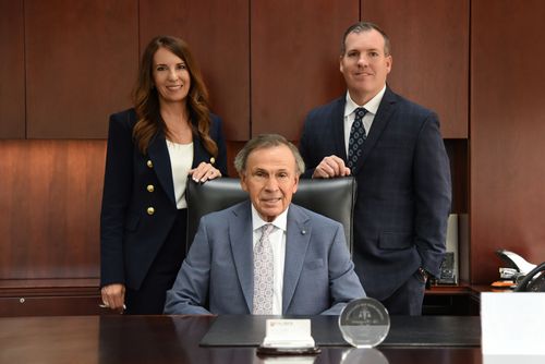 Three business people standing in front of a Tauber building, dressed in suits and business attire.