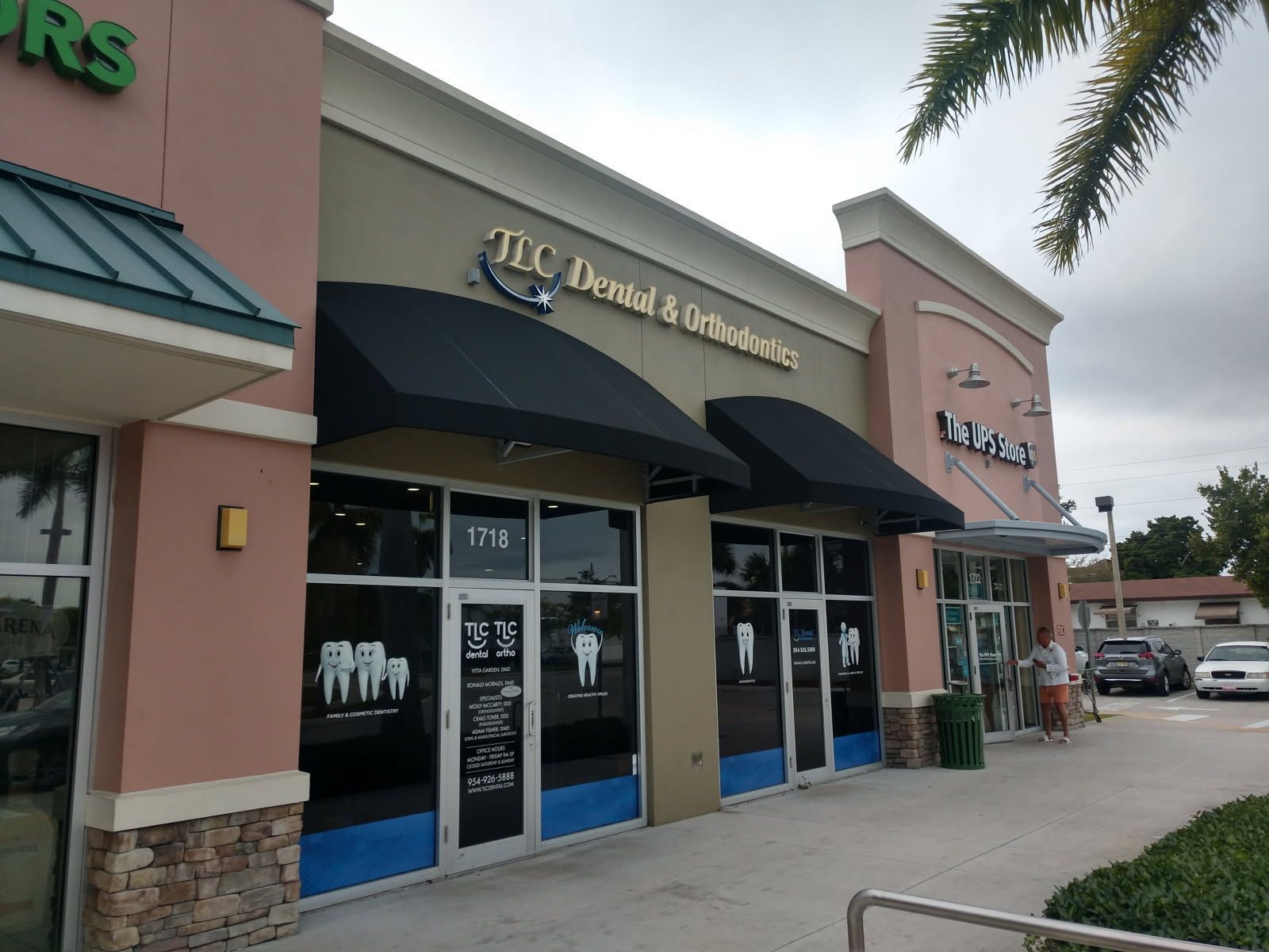 Strip mall storefronts with black awnings, including a dentistry office entrance on a sidewalk.