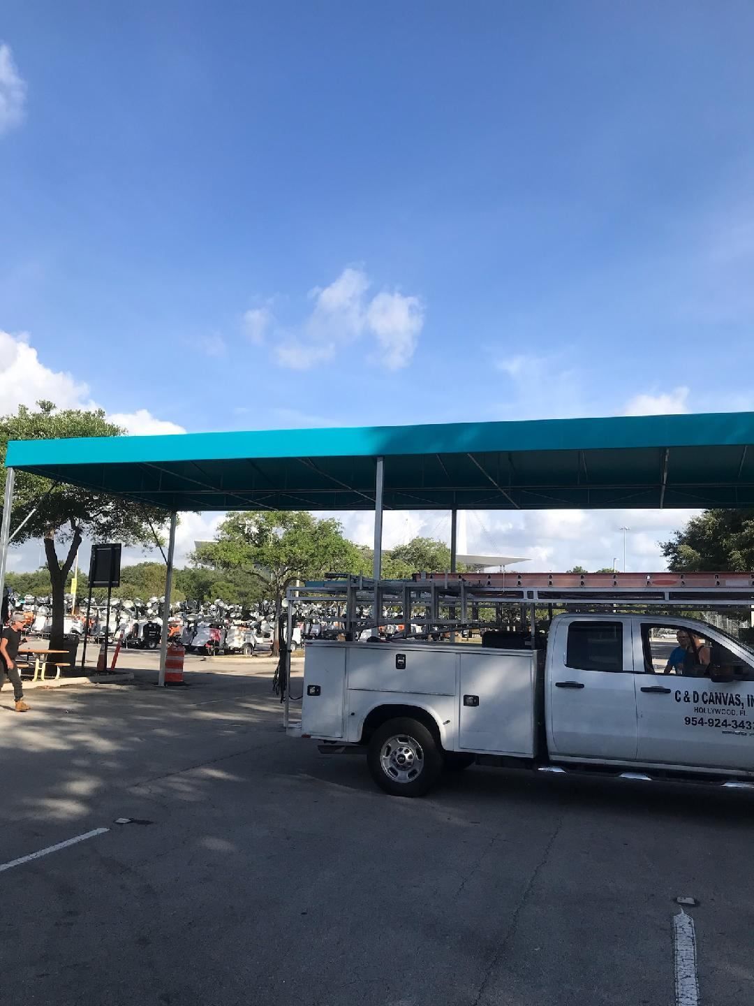 Covered parking lot with a white pickup truck under a teal canopy on a sunny day