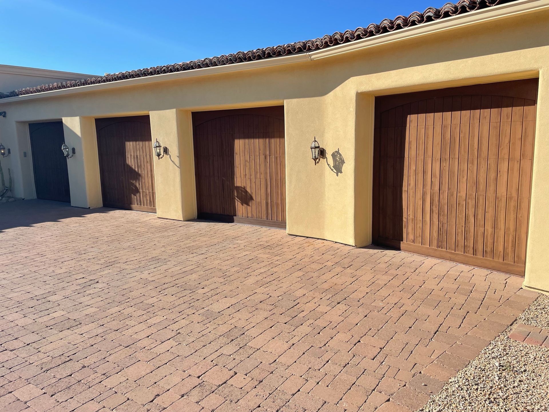 Row of tan stucco garage bays with brown wood doors on brick paved driveway.