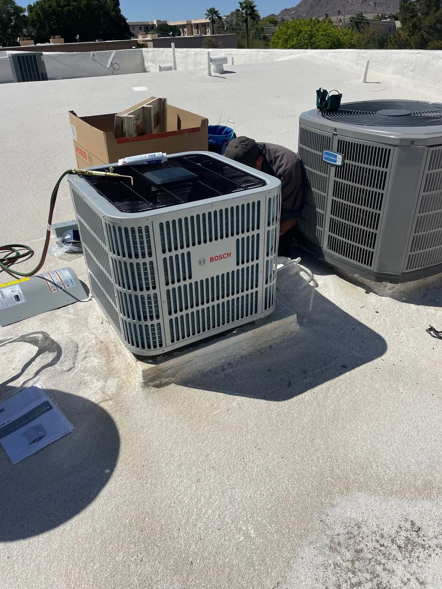 HVAC technician working on rooftop air conditioning units. Brown box, tools, bright sunlight.