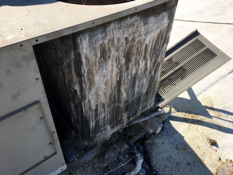 Exterior of HVAC unit with water and debris stains, mounted on a concrete surface.