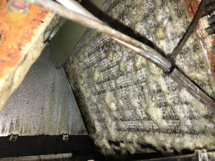 A heavily soiled HVAC coil with thick, white, and dark buildup in a metal housing.