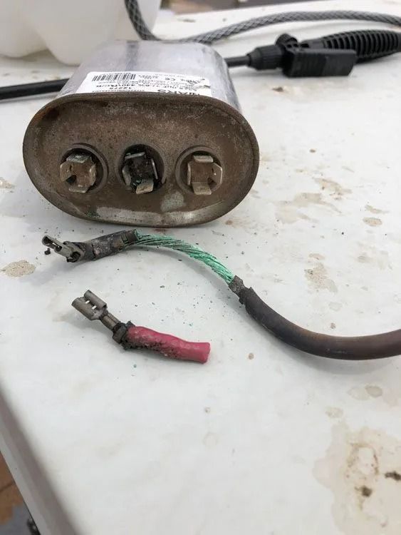 Damaged electrical capacitor with burnt wires and connectors on a white surface.