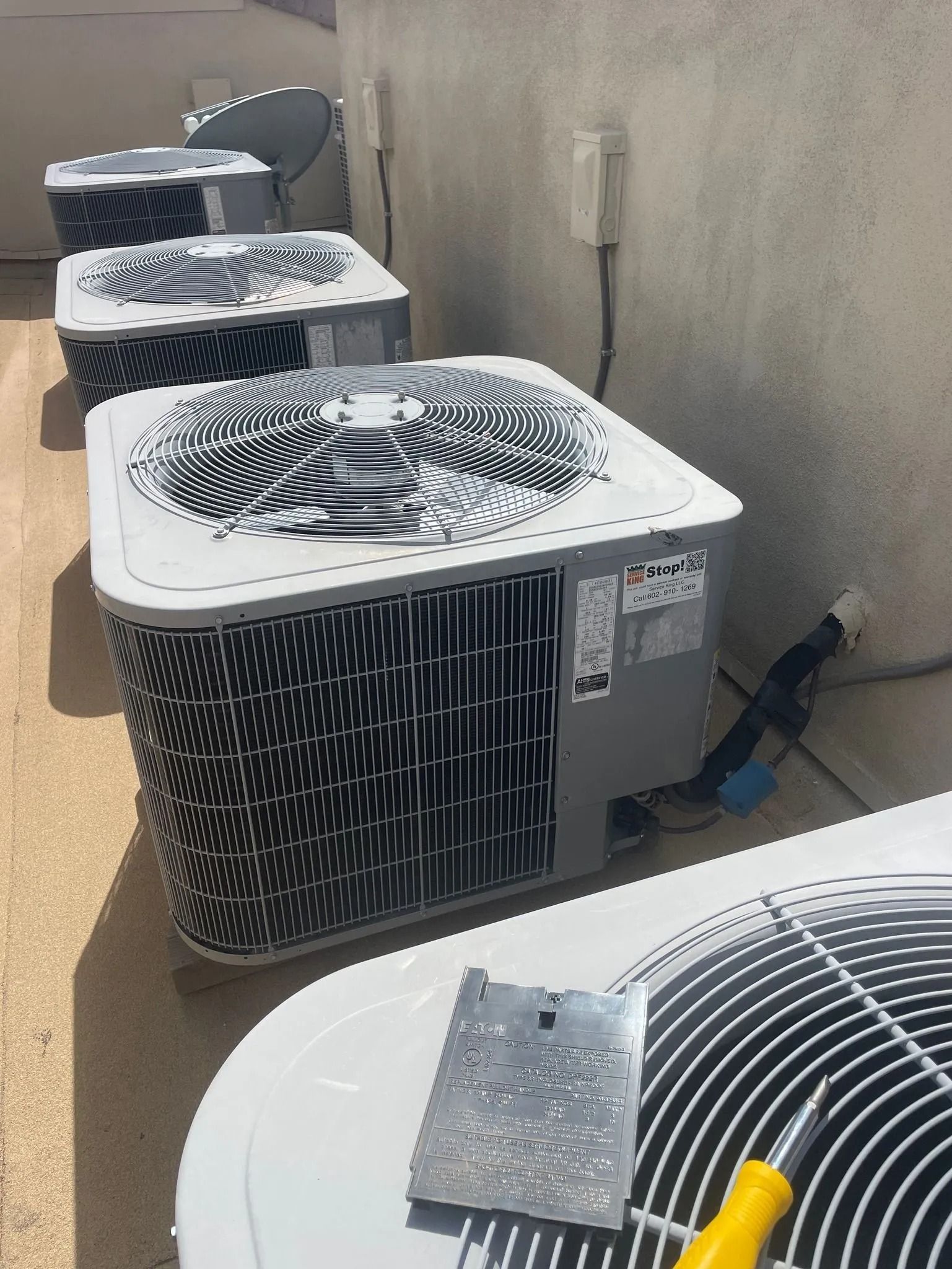 Several air conditioning units lined up on a rooftop; tools are in front of the closest unit.