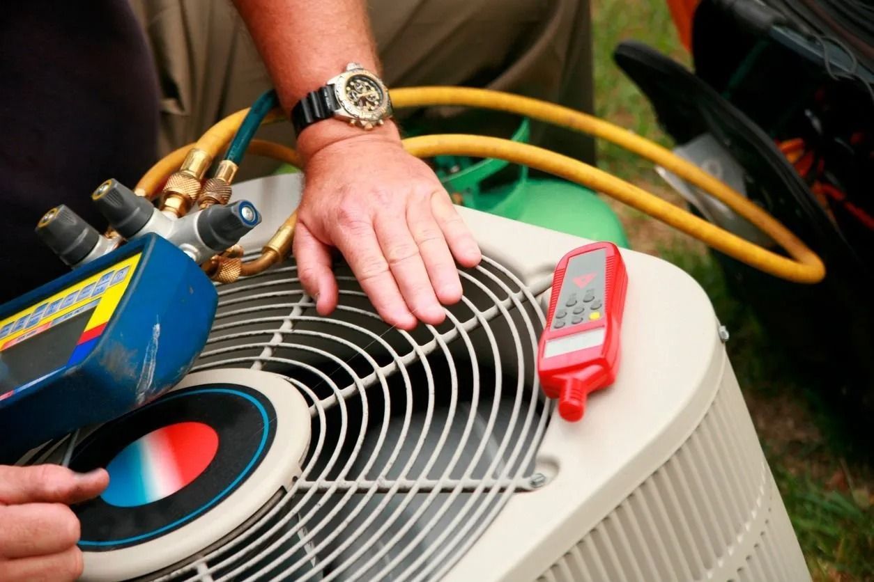 Person's hand on AC unit, connected to gauges.  Checking the system with a temperature reader.  Yellow hose and green tank visible.