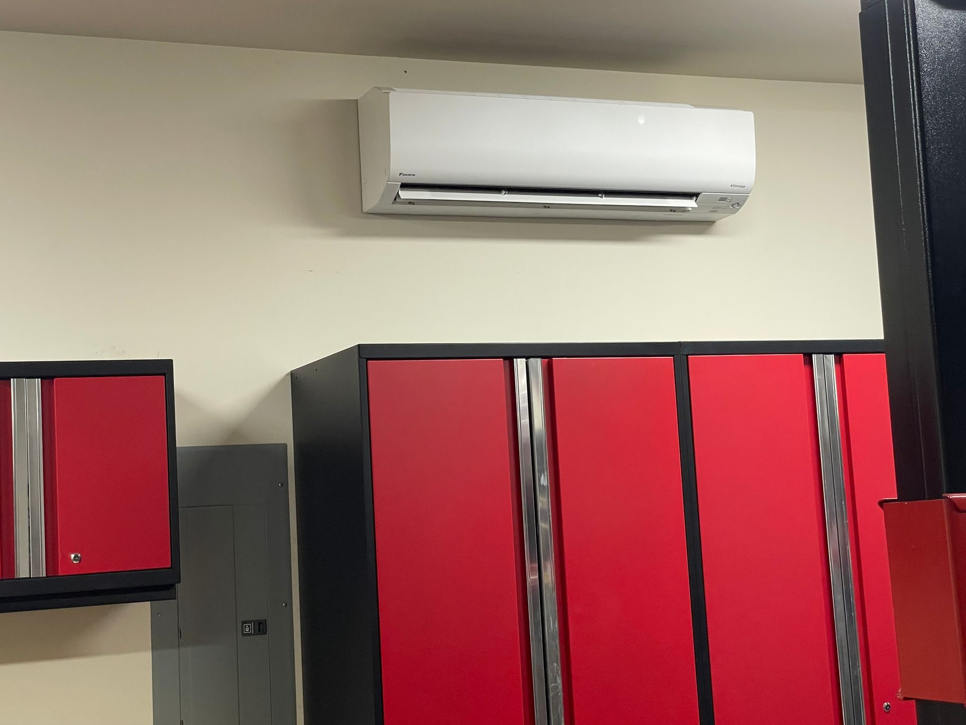 White air conditioner above red and black cabinets on a beige wall.