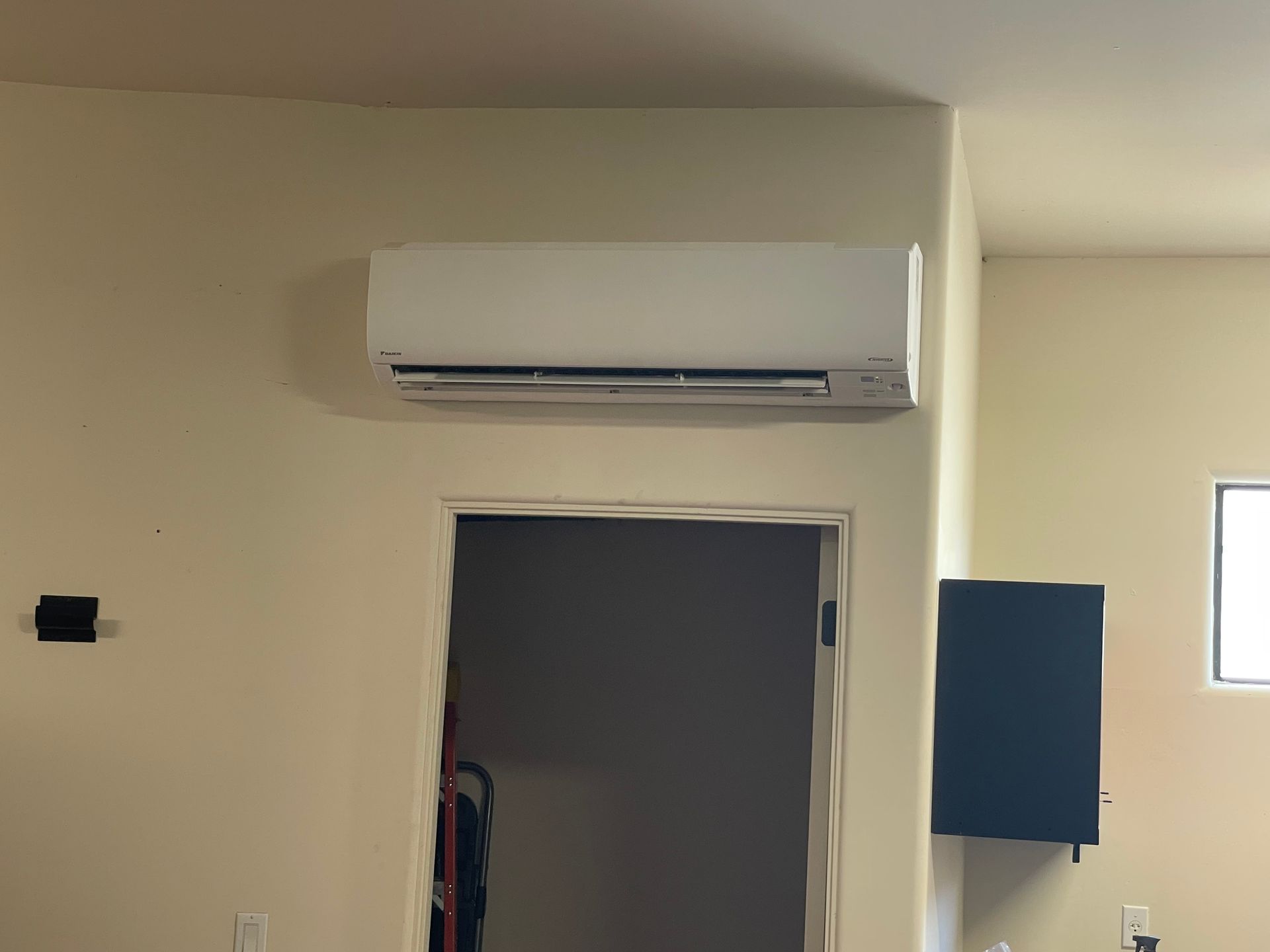 White air conditioning unit mounted above a doorway in a room with beige walls.