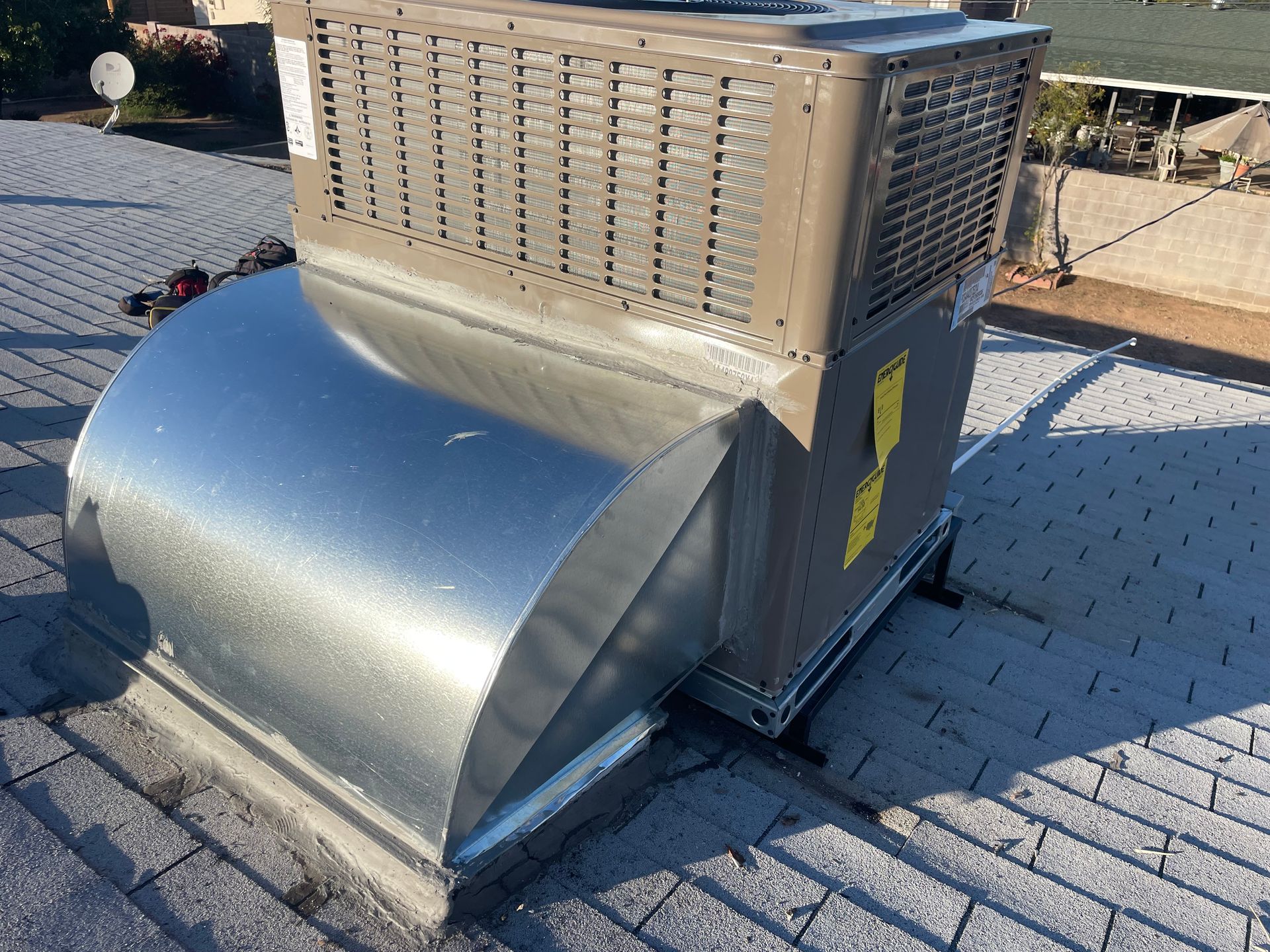 Rooftop HVAC unit with metallic ductwork on a shingled roof.