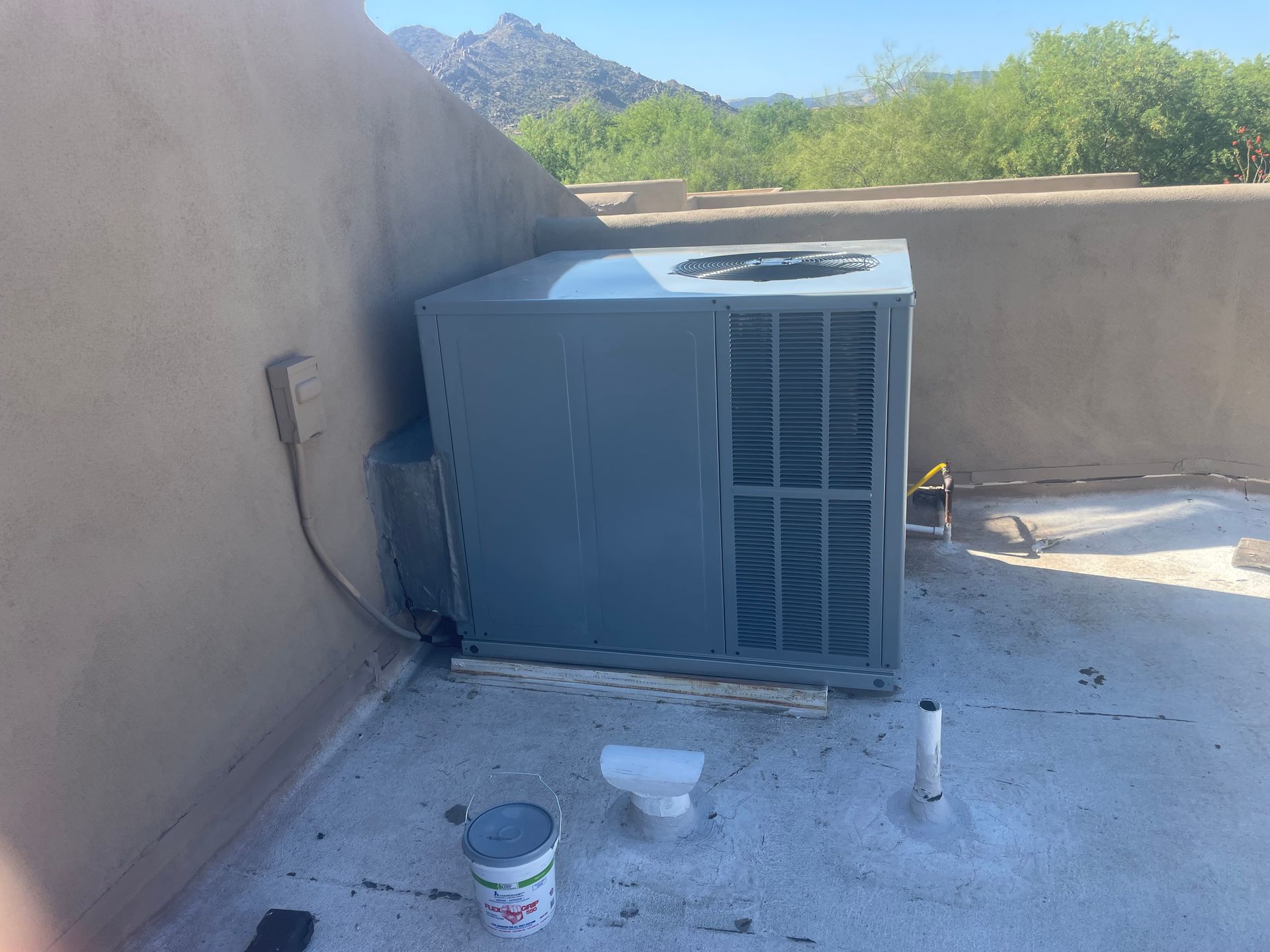 Air conditioning unit on a flat roof with a mountainous backdrop.