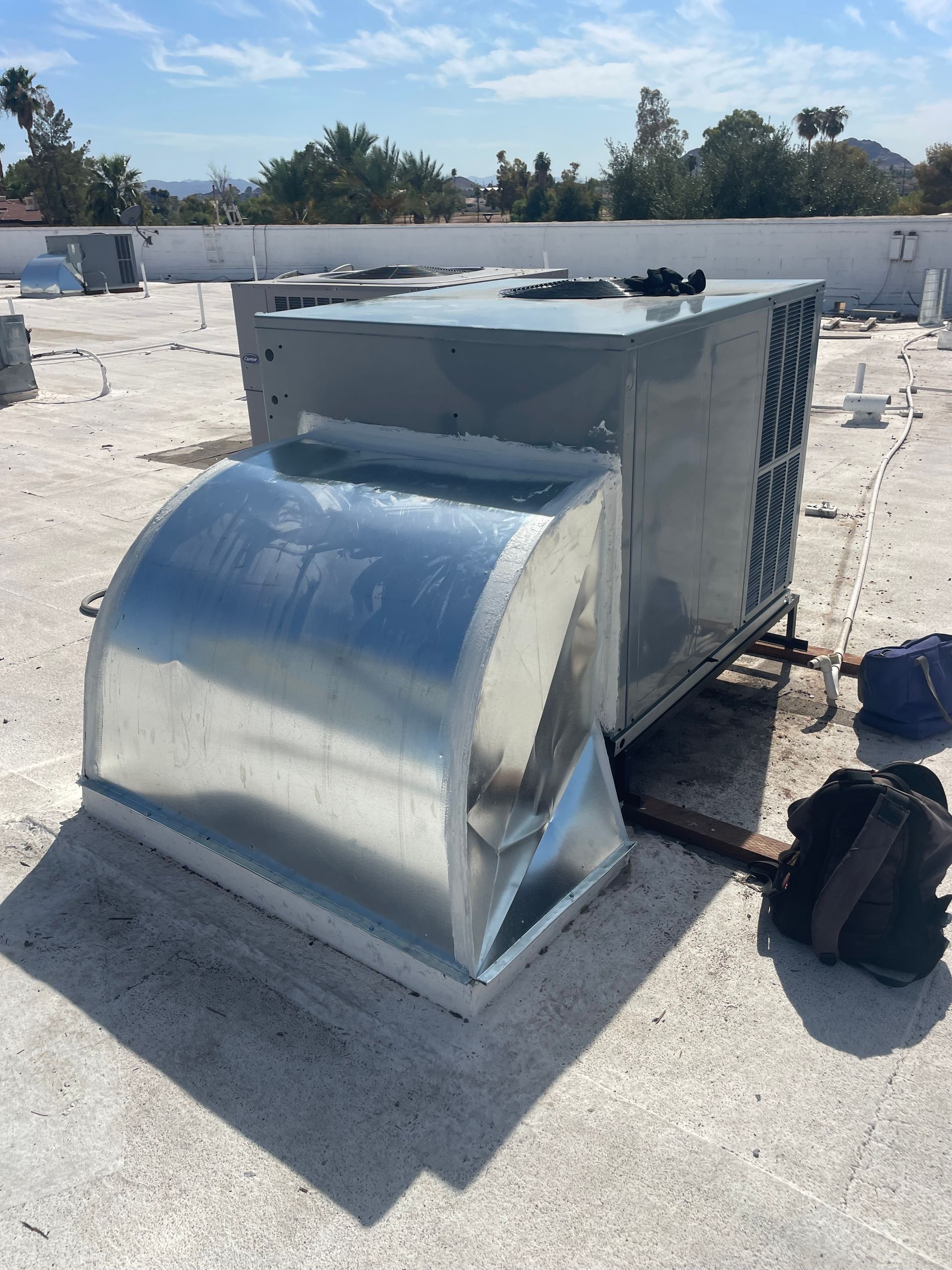 Rooftop air conditioning unit with silver ductwork, under a bright, sunny sky.