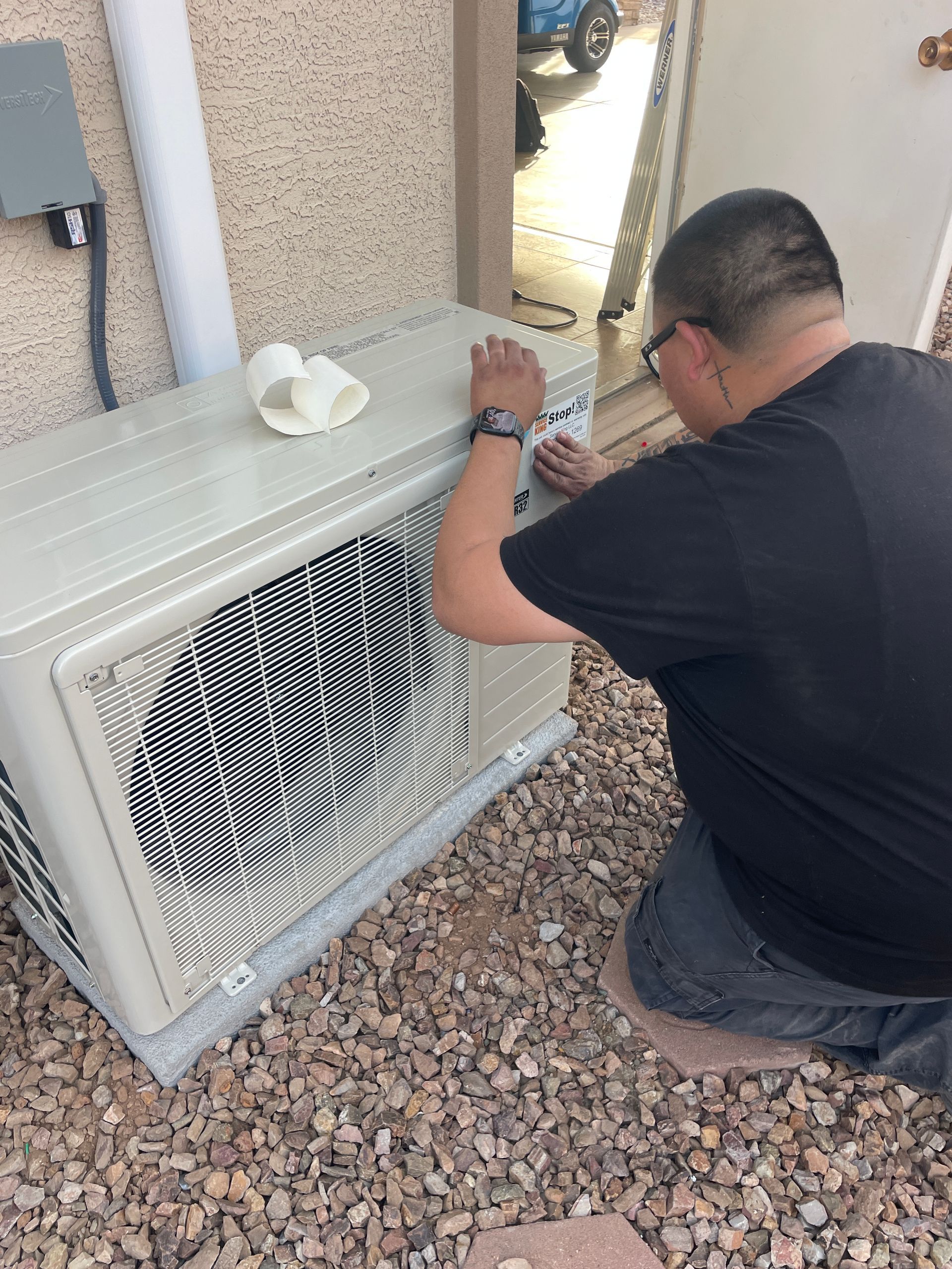 A person kneeling, working on an outdoor air conditioning unit.