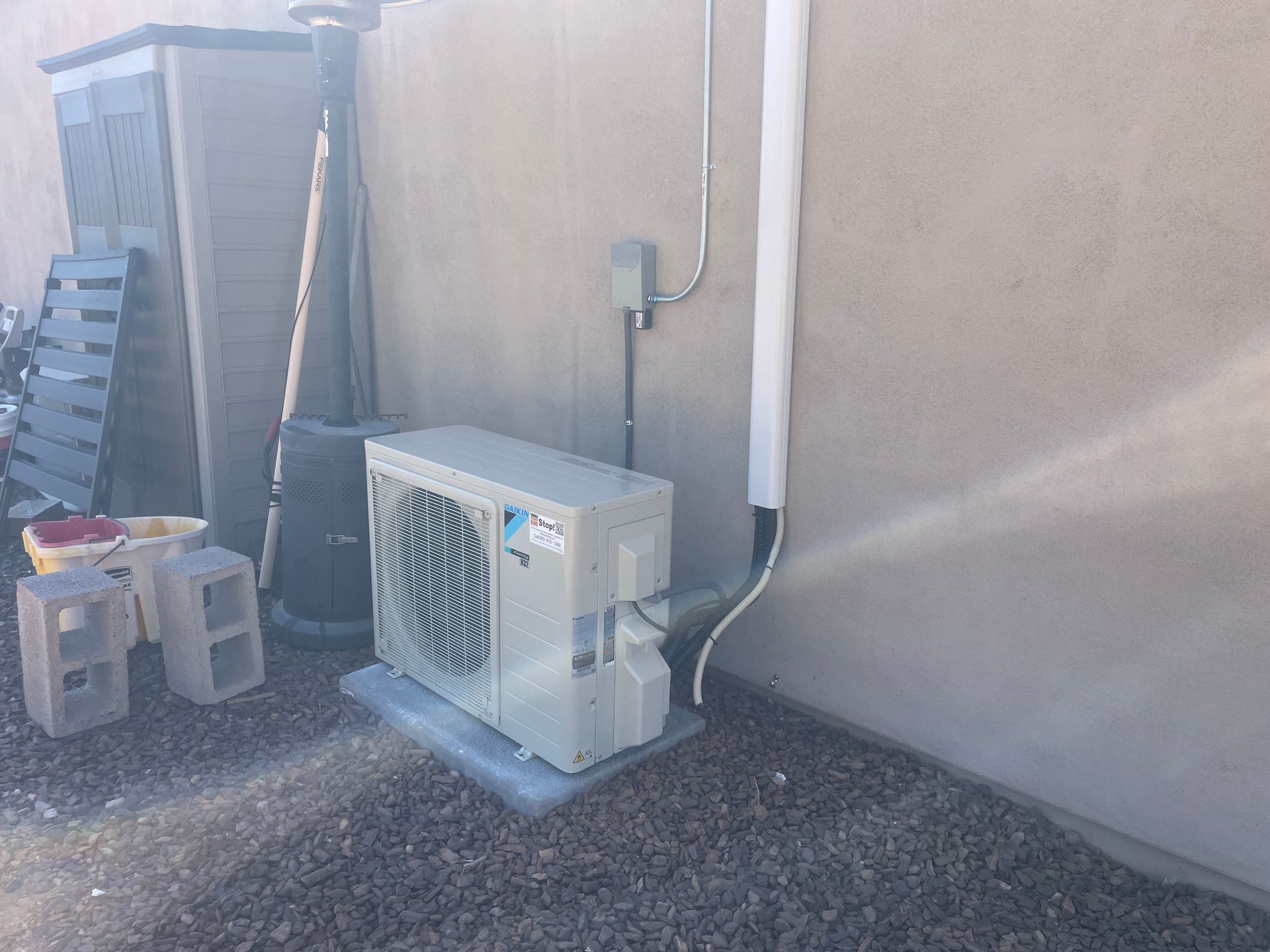 An air conditioning unit sits on a concrete pad next to a light-colored stucco wall.