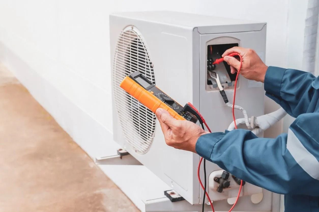 Person in blue overalls tests an AC unit's electrical components with a multimeter outdoors.