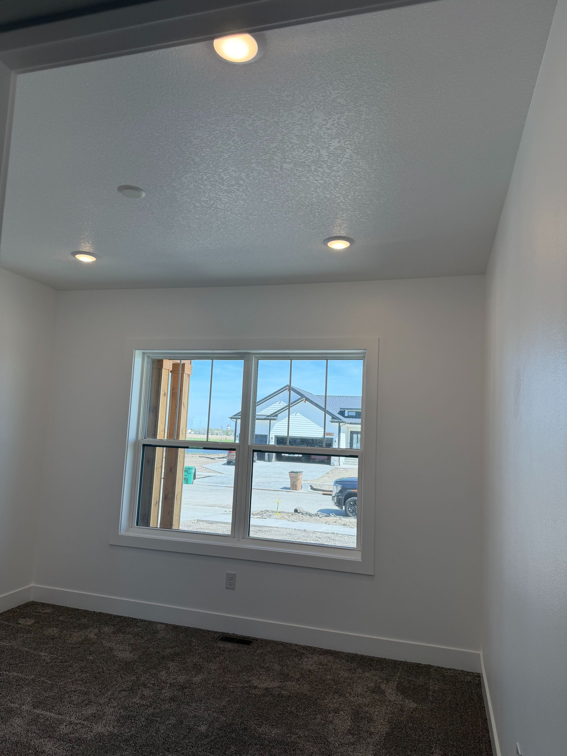 Empty white bedroom with ceiling lights, window, and dark carpet, showing a construction site outside