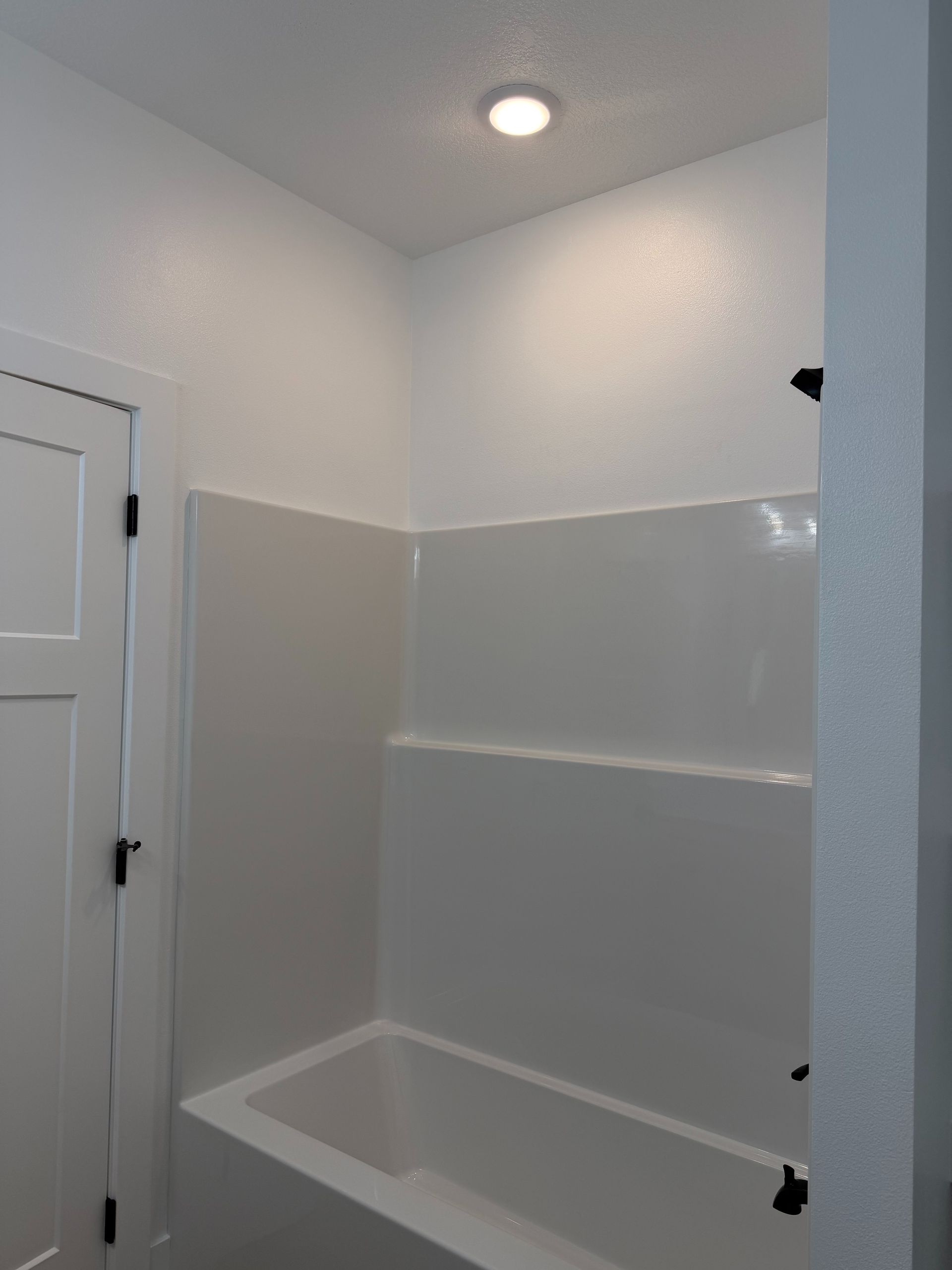 Bathroom shower alcove with white tile, gray upper walls, and a recessed ceiling light