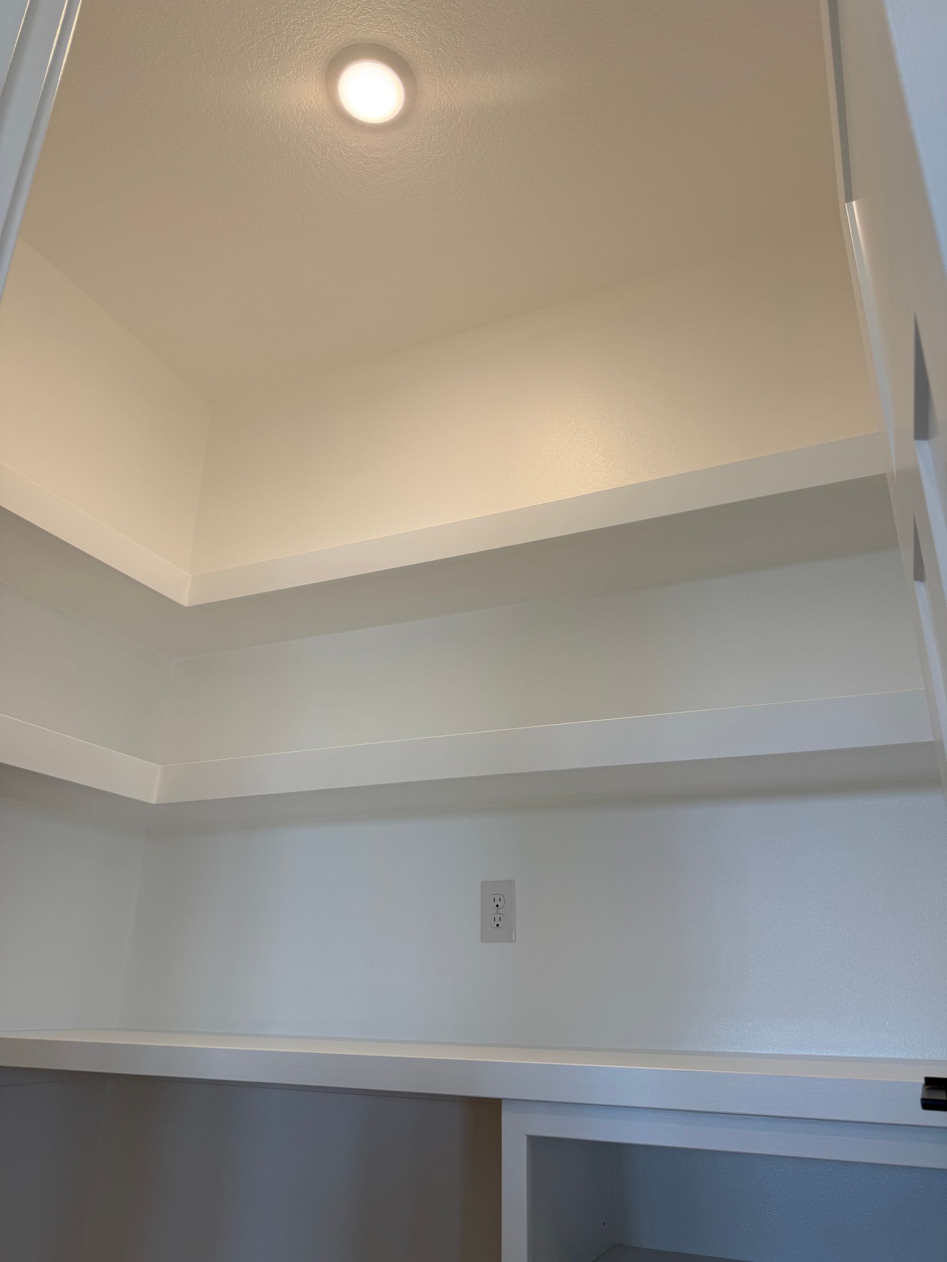 Empty built-in closet with white shelves and a recessed light in the ceiling.