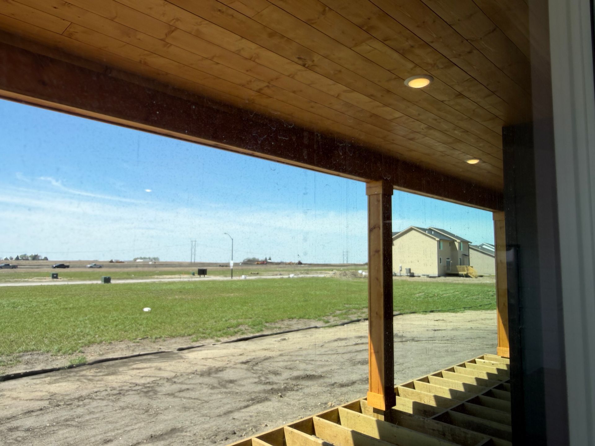 Covered porch overlooking a grassy field and distant buildings under a wooden roof