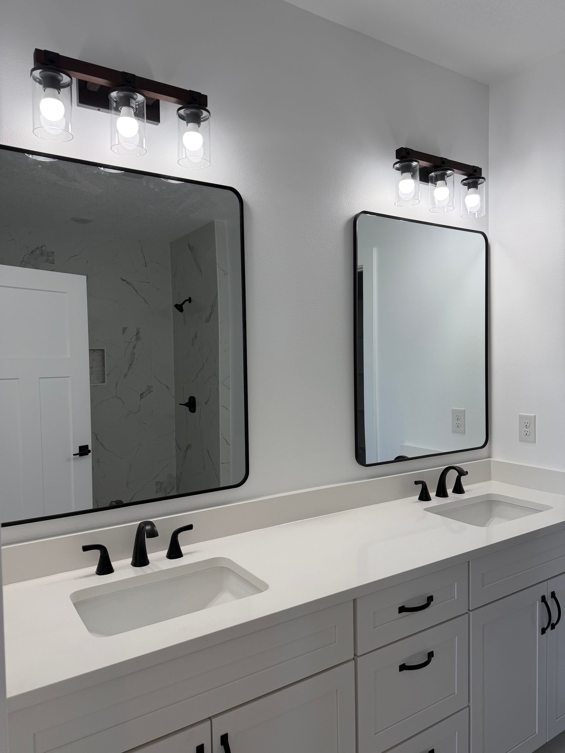 Modern bathroom vanity with two mirrors, black fixtures, white countertop, and wall-mounted lights.