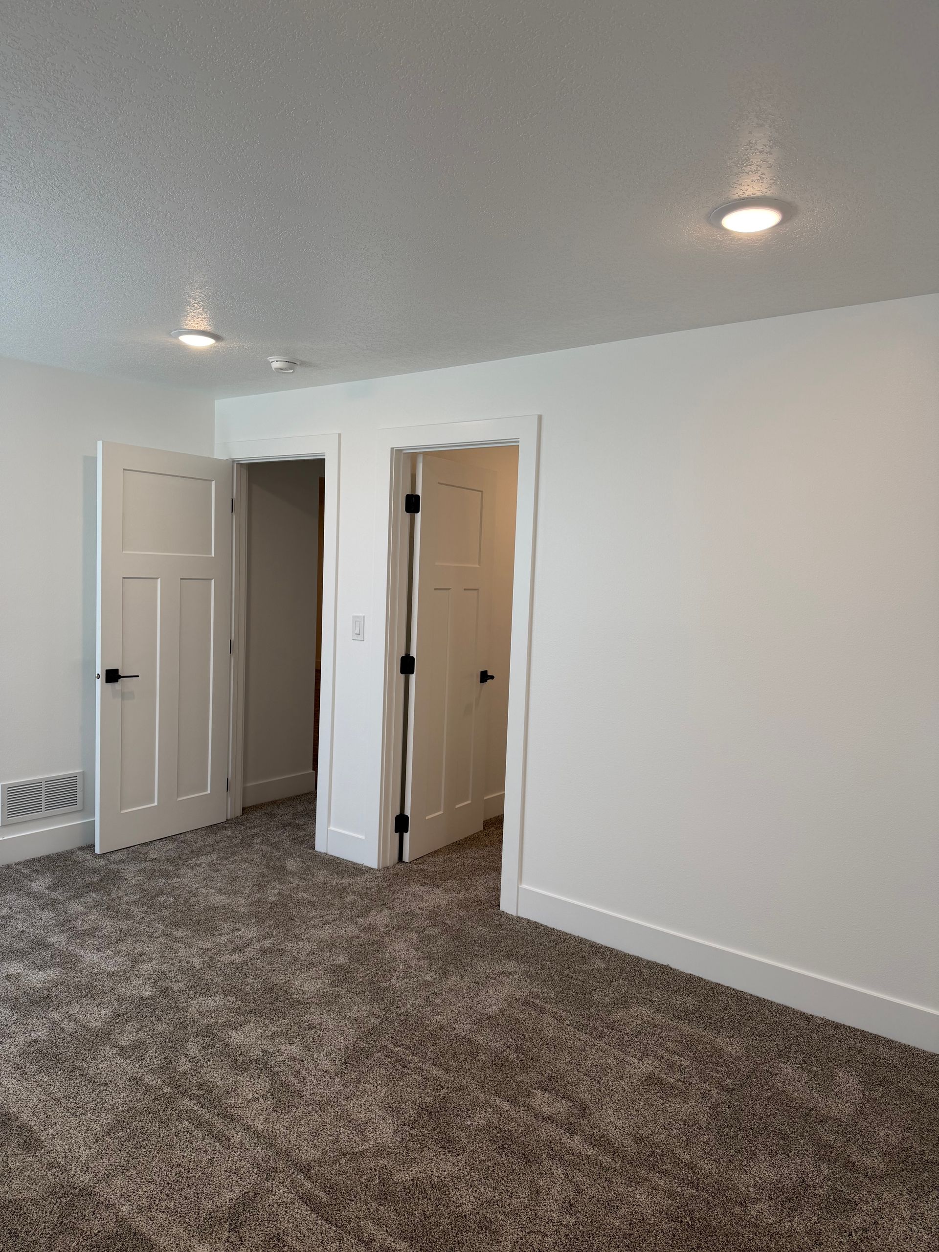 Empty carpeted room with white walls, open closet doors, and ceiling lights