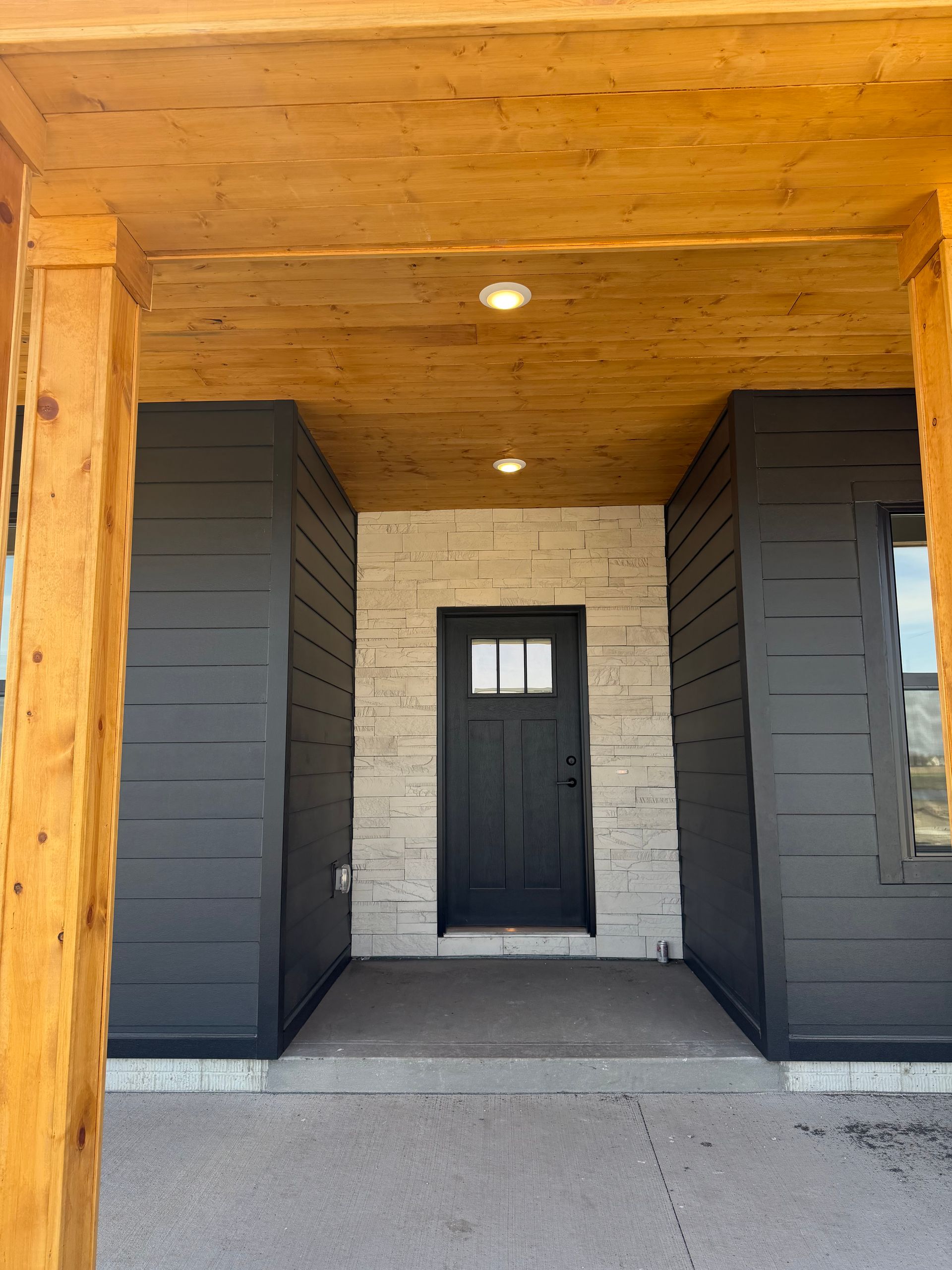 Covered front entrance with black door, white brick wall, and dark wood beams.