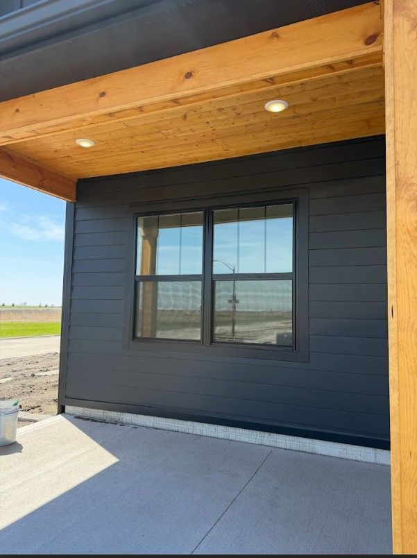 Modern black house exterior with a window beneath a wood porch ceiling