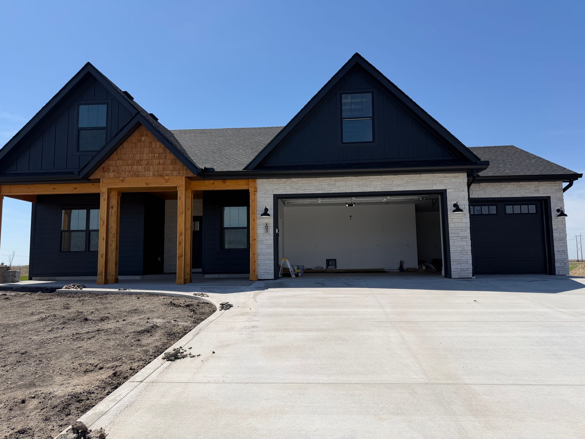 New suburban house with dark gables, brick and white siding, and a two-car garage under construction