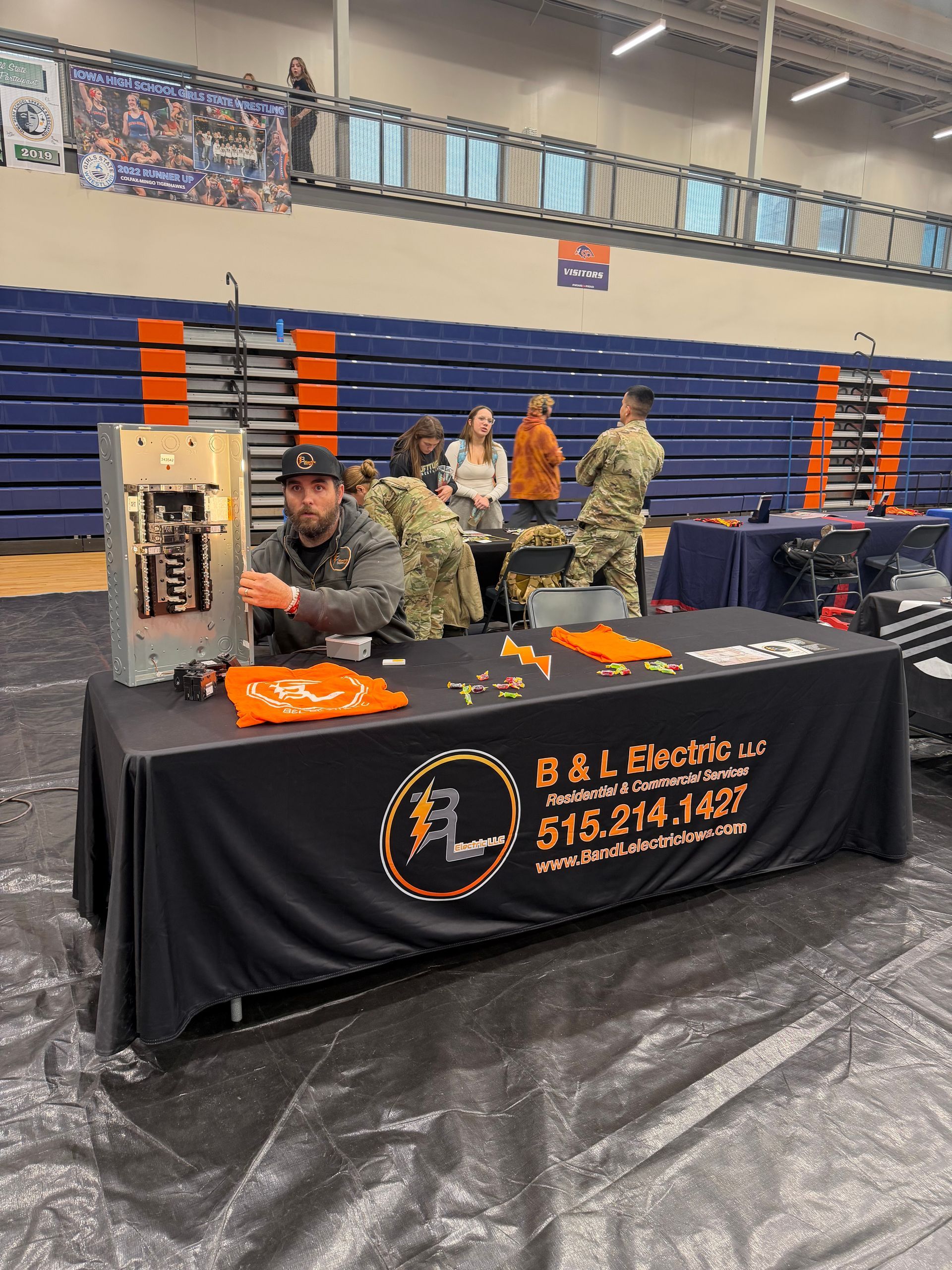 Electrical company booth. A man is working on a panel at a table with the company logo. Others in the background.