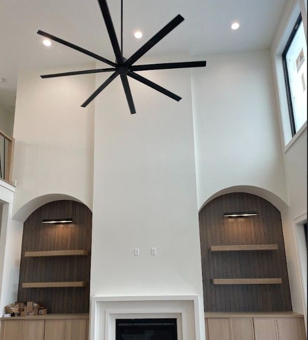 High-ceiling living room with a black ceiling fan, fireplace, built-in shelves, and windows.